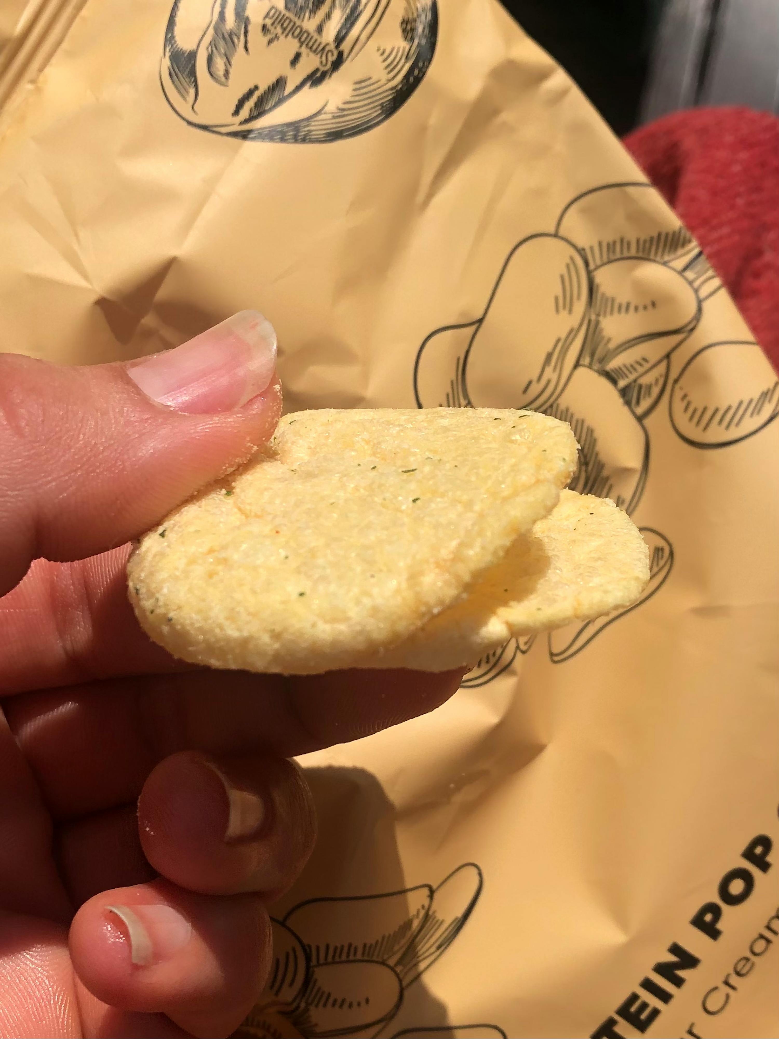 a person is holding a potato chip in front of a bag that says protein pop