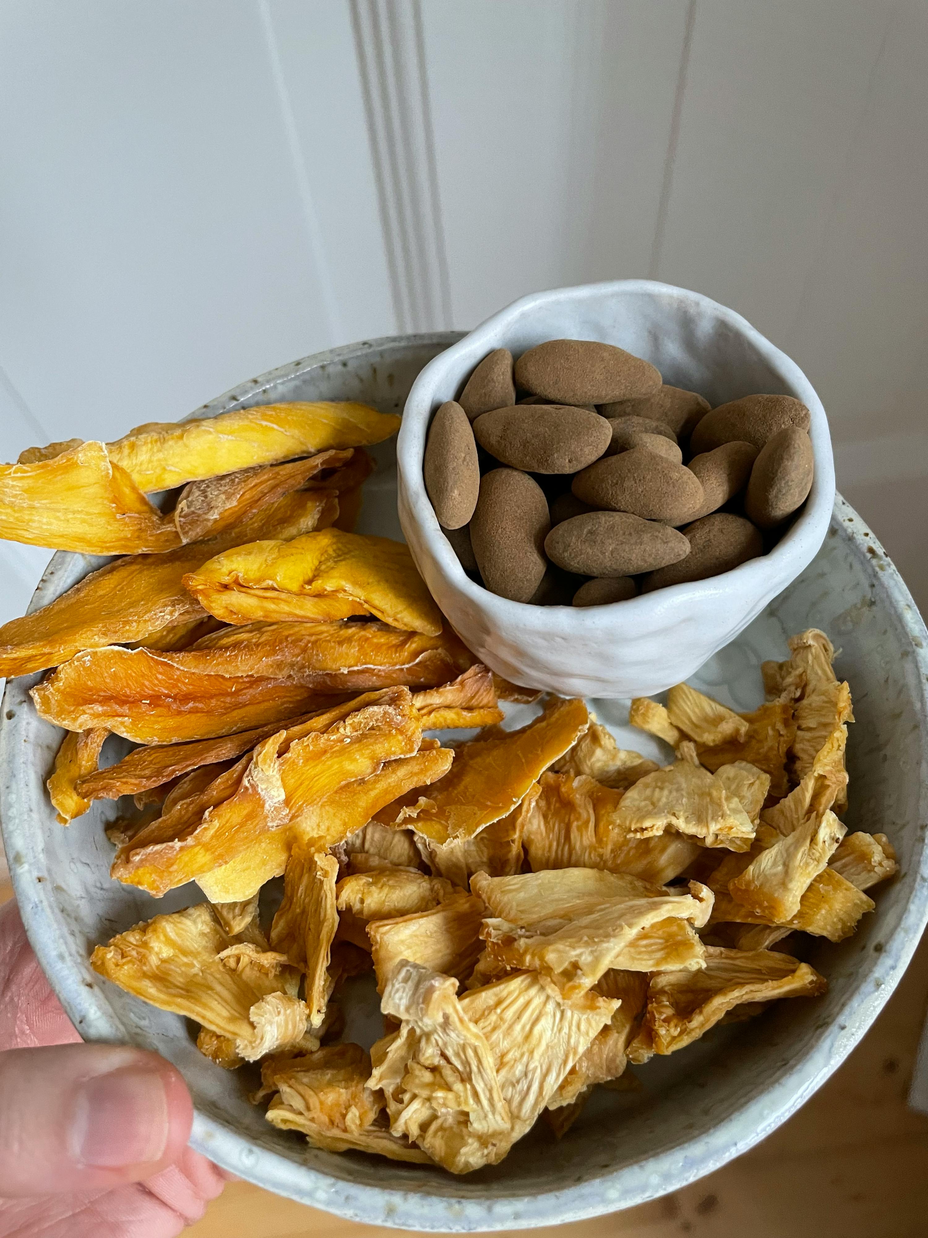 eine Person hält einen Teller mit getrockneten Früchten und Mandeln