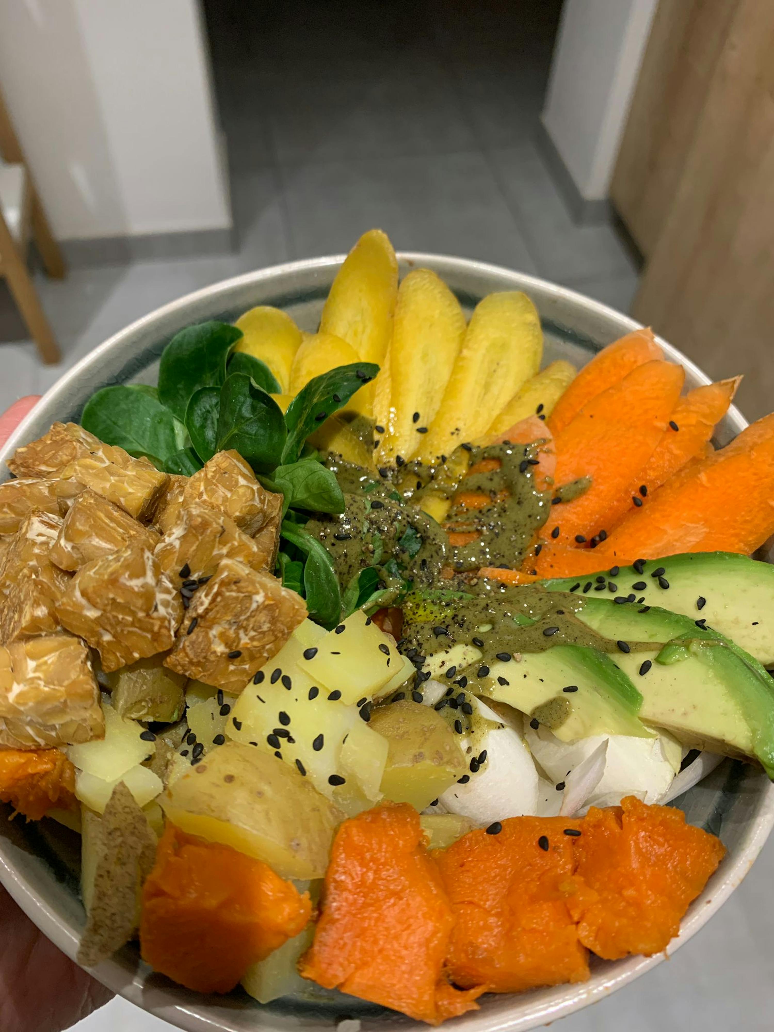 a person is holding a bowl of vegetables including avocado and carrots