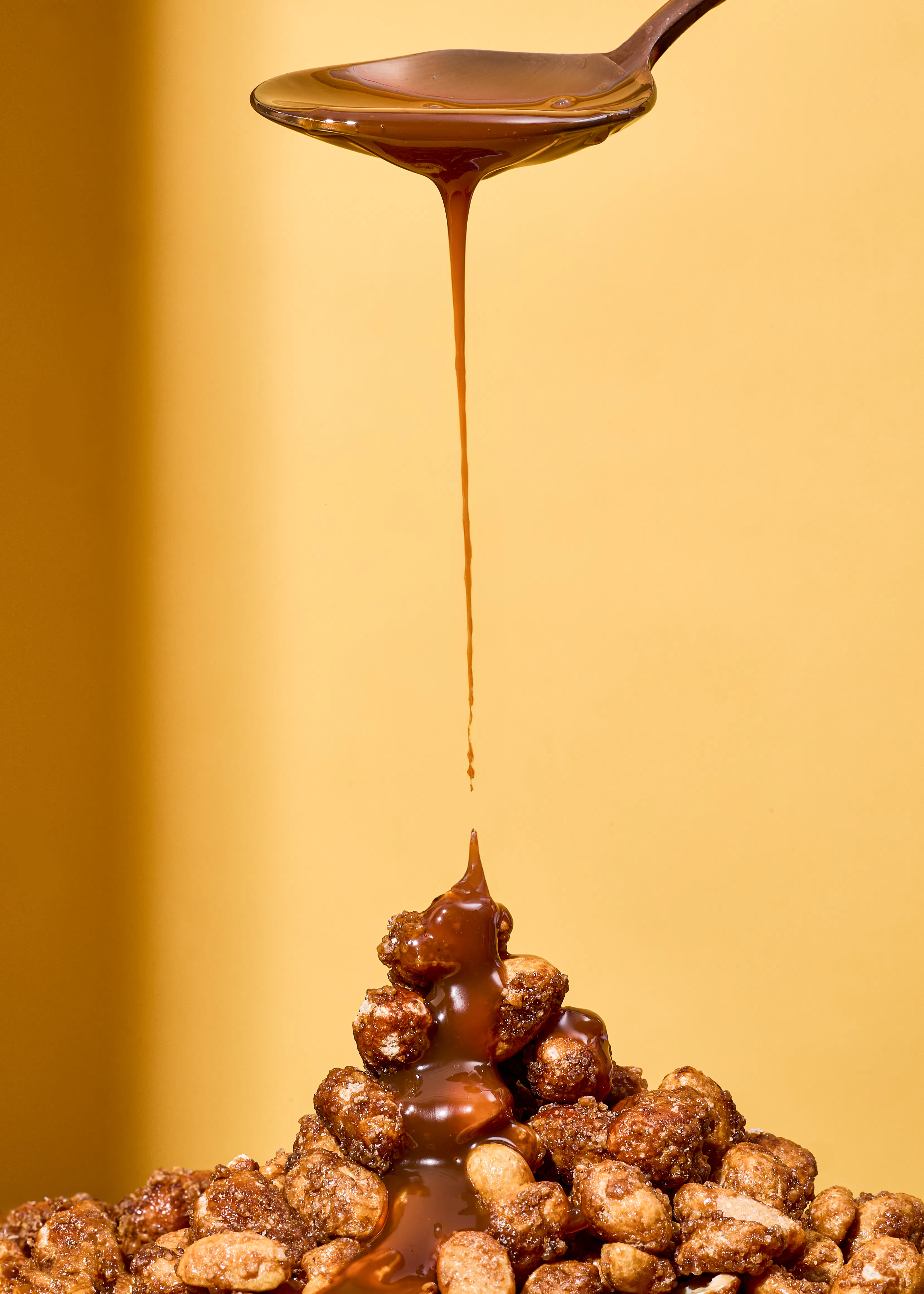Karamellsauce wird aus einem Löffel auf einen Haufen Erdnüsse gegossen