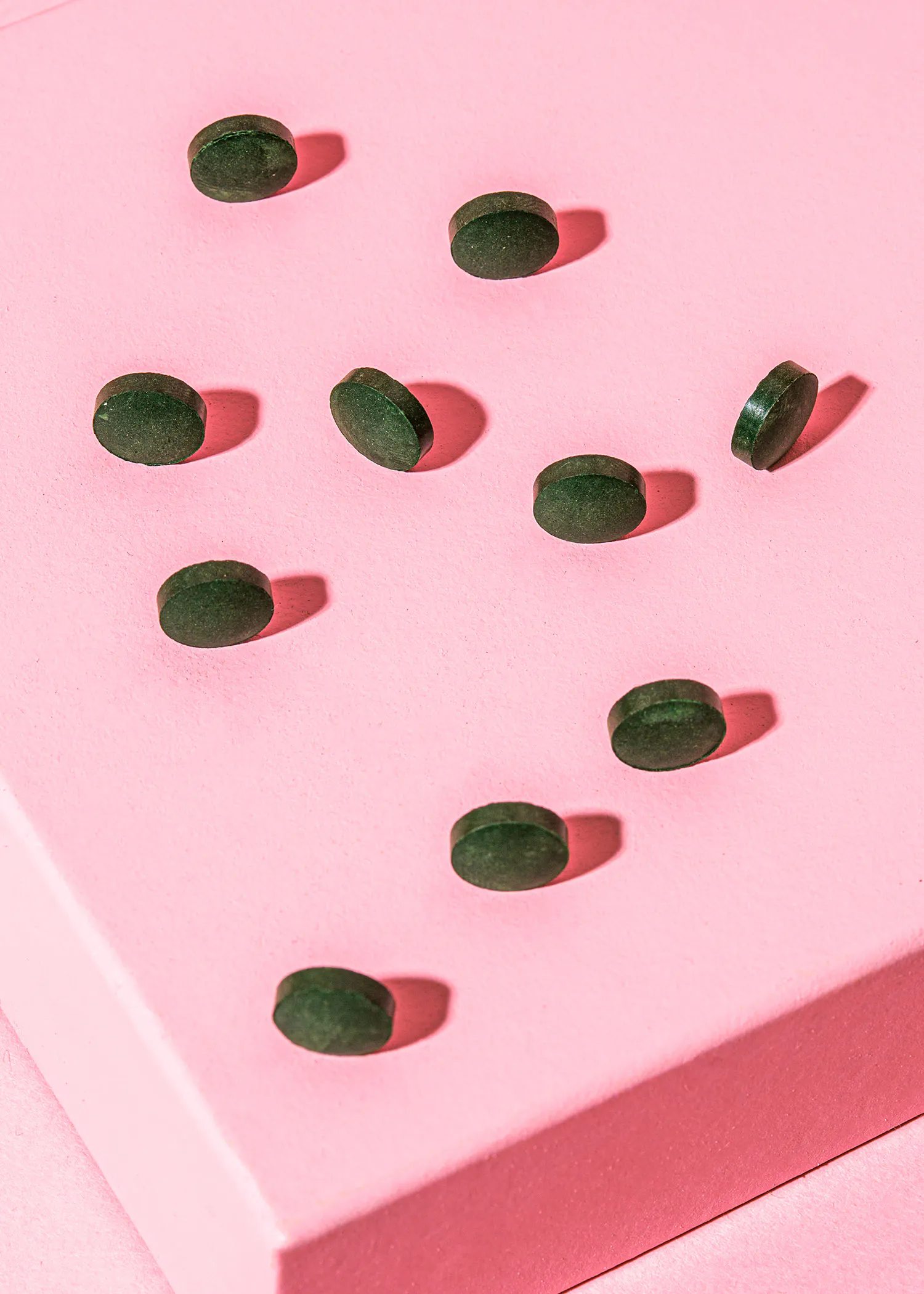 green pills are lined up on a pink surface