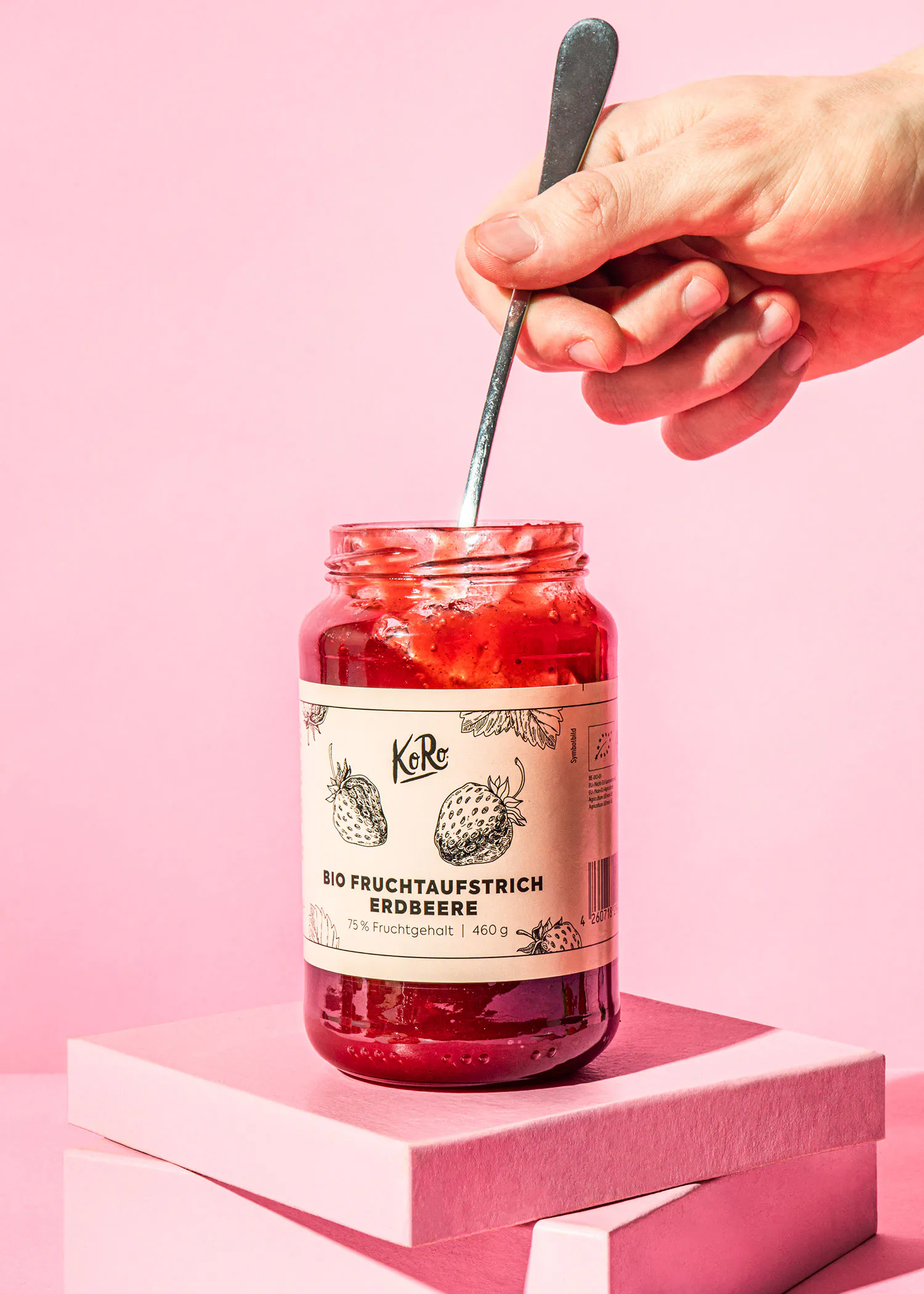 une personne tient une cuillère à côté d' un pot de confiture de fraises