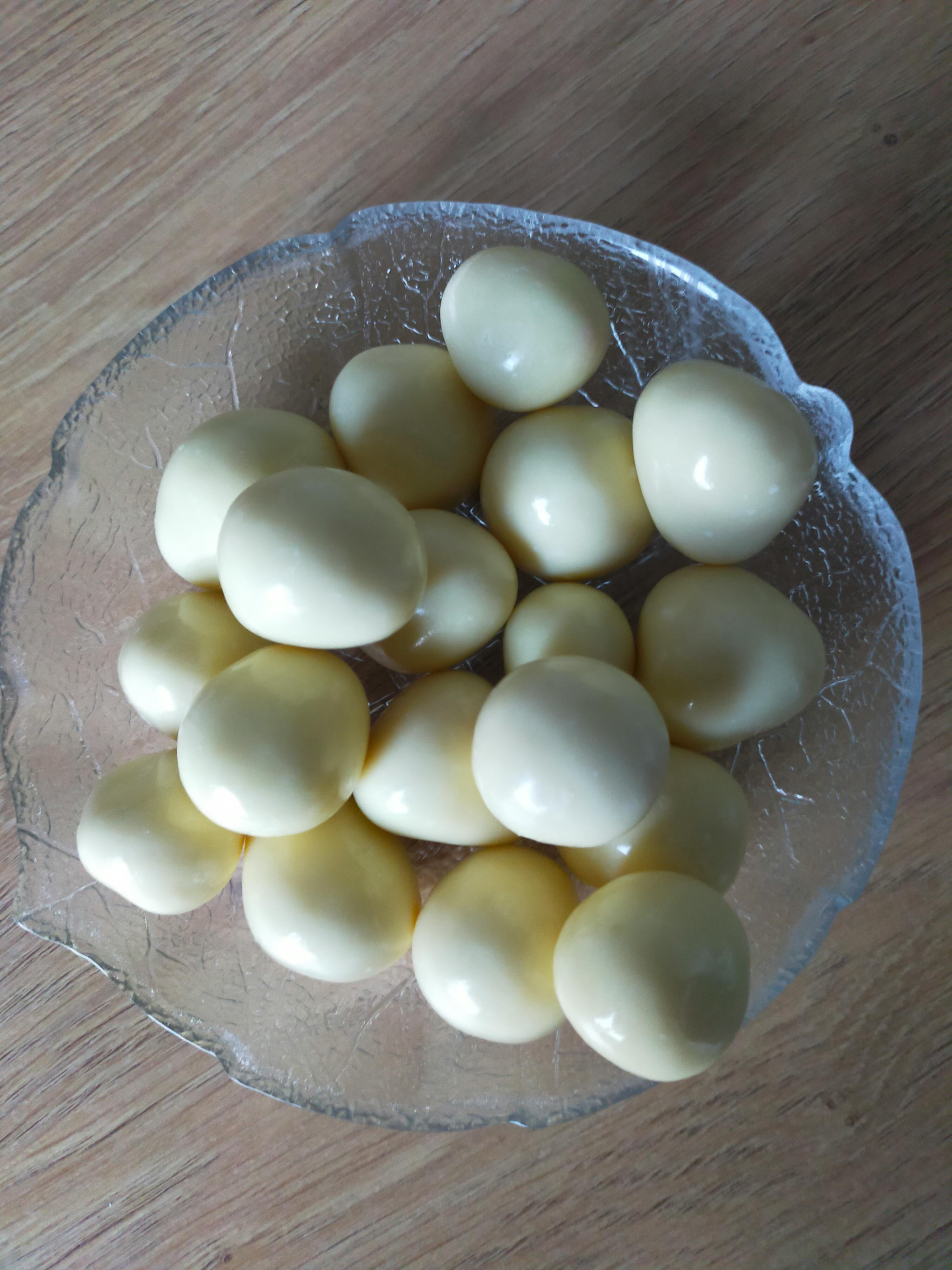 eine glasschale gefüllt mit vielen kleinen, runden, cremefarbenen bonbons auf einem holztisch.
