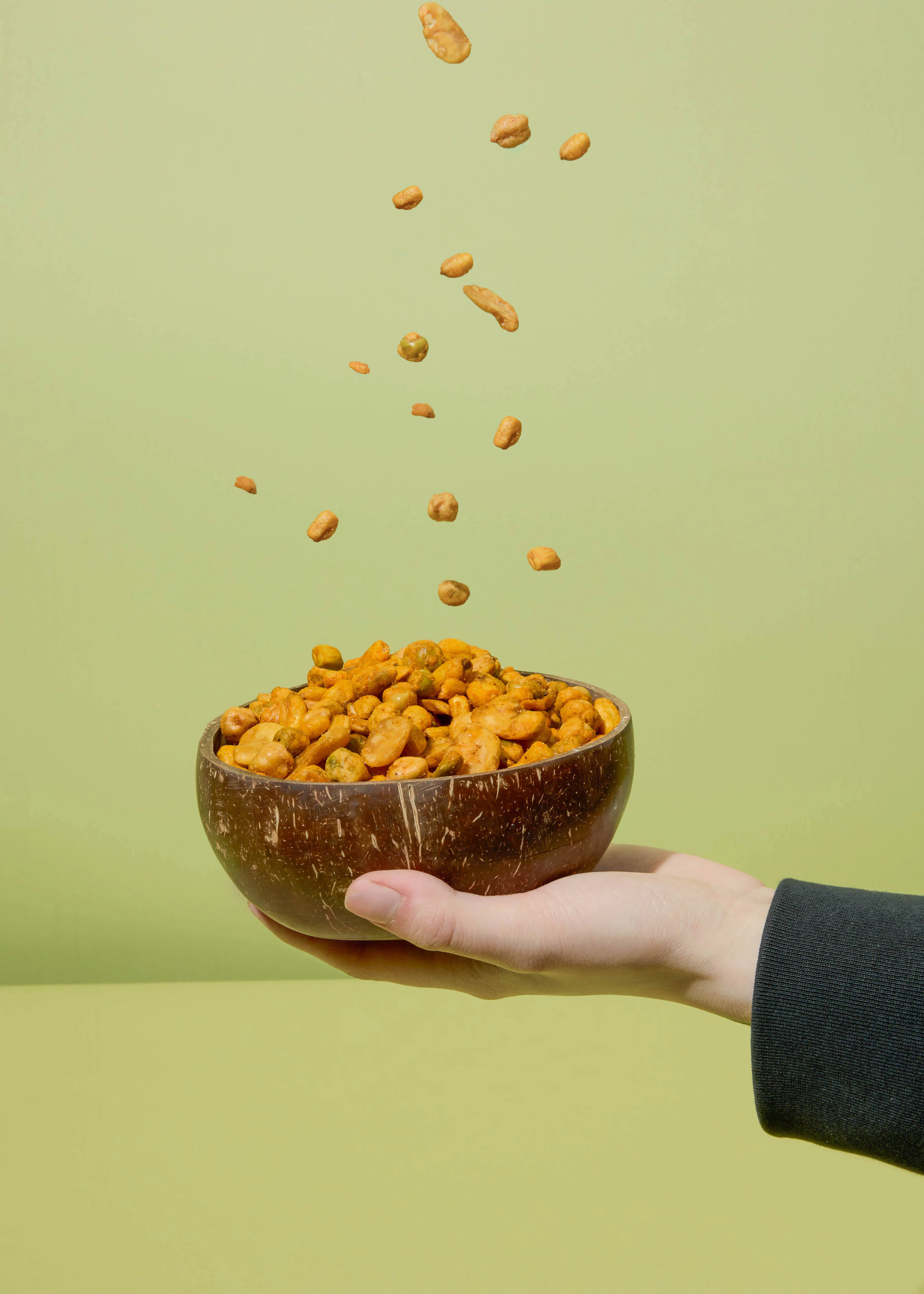 a hand holding a bowl of peanuts with peanuts falling into it