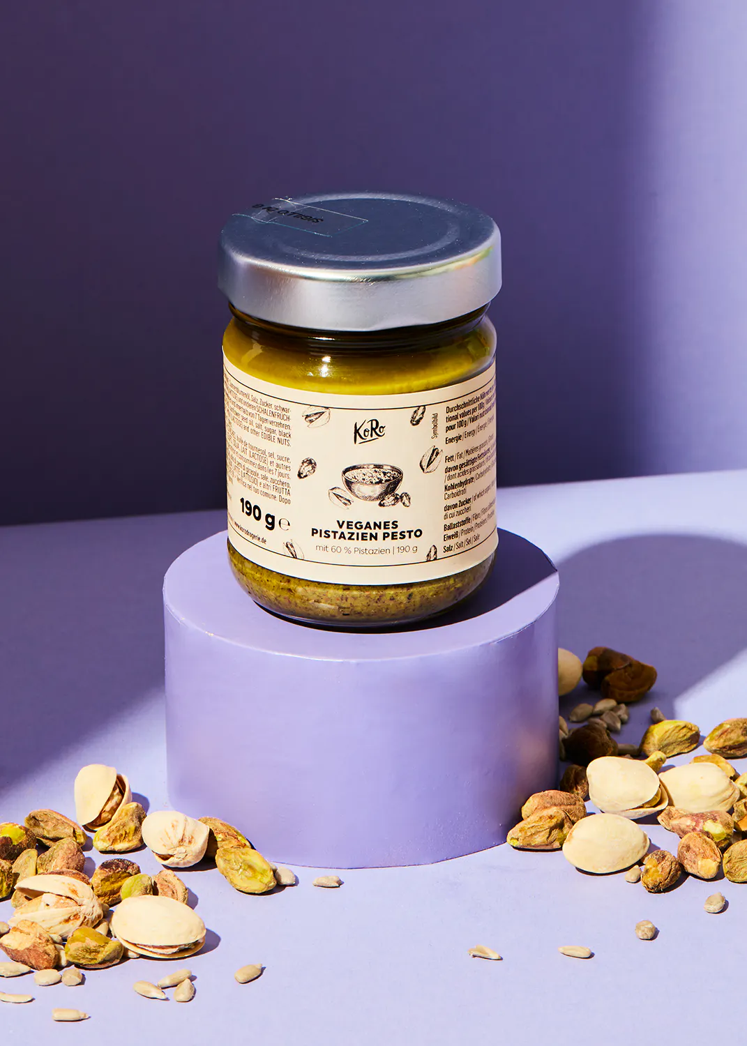 un bocal de pesto végétalien est posé sur un support violet entouré de pistaches