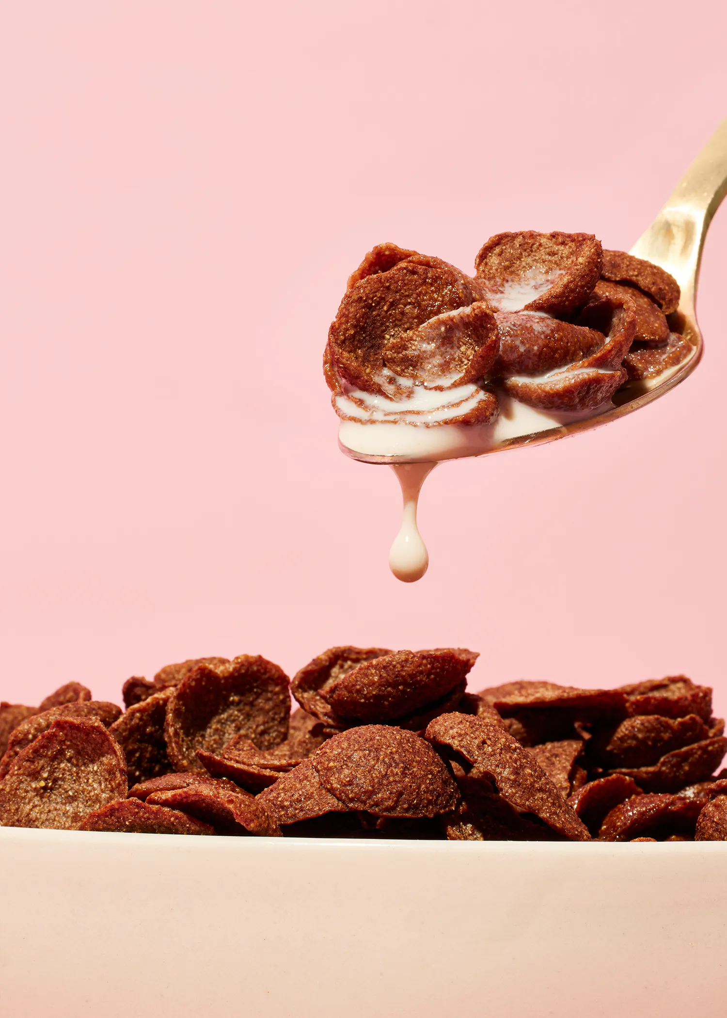 une cuillère remplie de céréales au chocolat et de lait sur fond rose