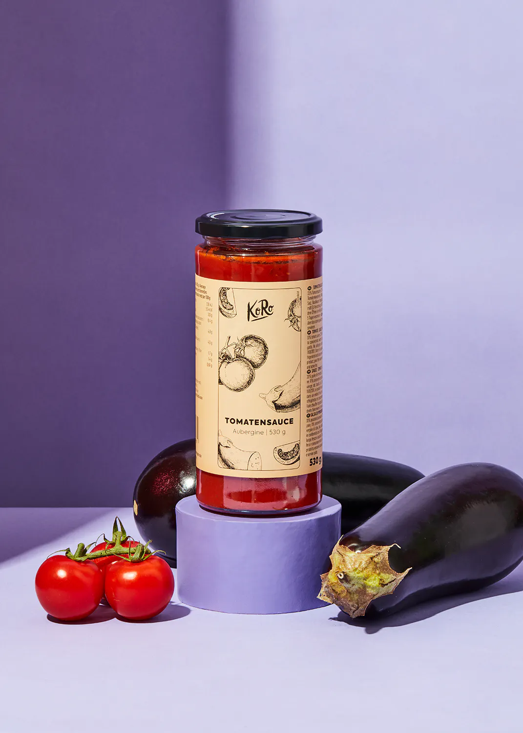 une bouteille de sauce tomate est posée sur un support violet à côté d' une aubergine et de tomates
