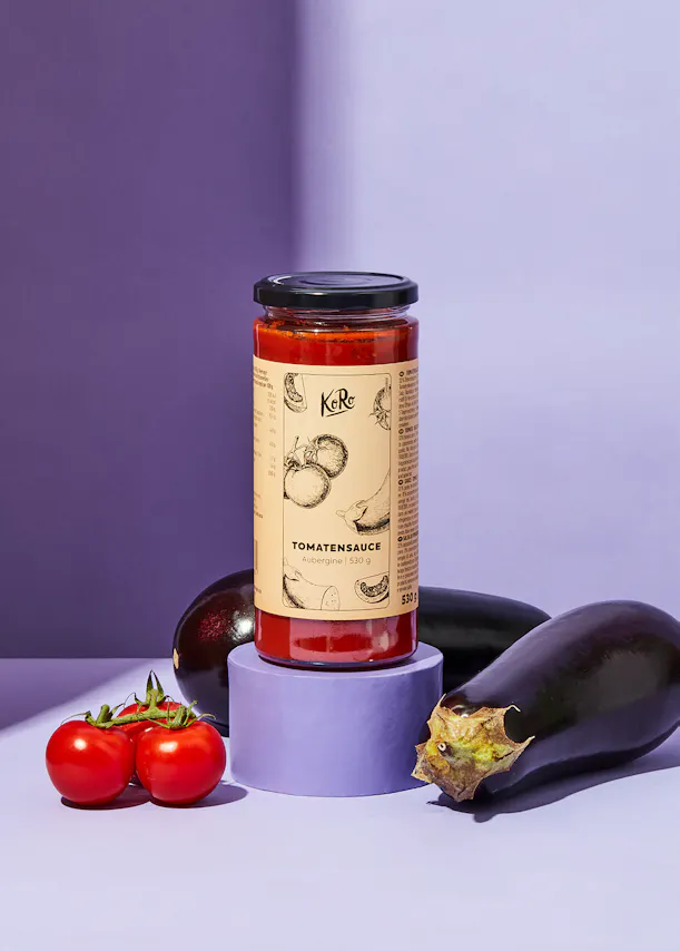 une bouteille de sauce tomate est posée sur un support violet à côté d' une aubergine et de tomates