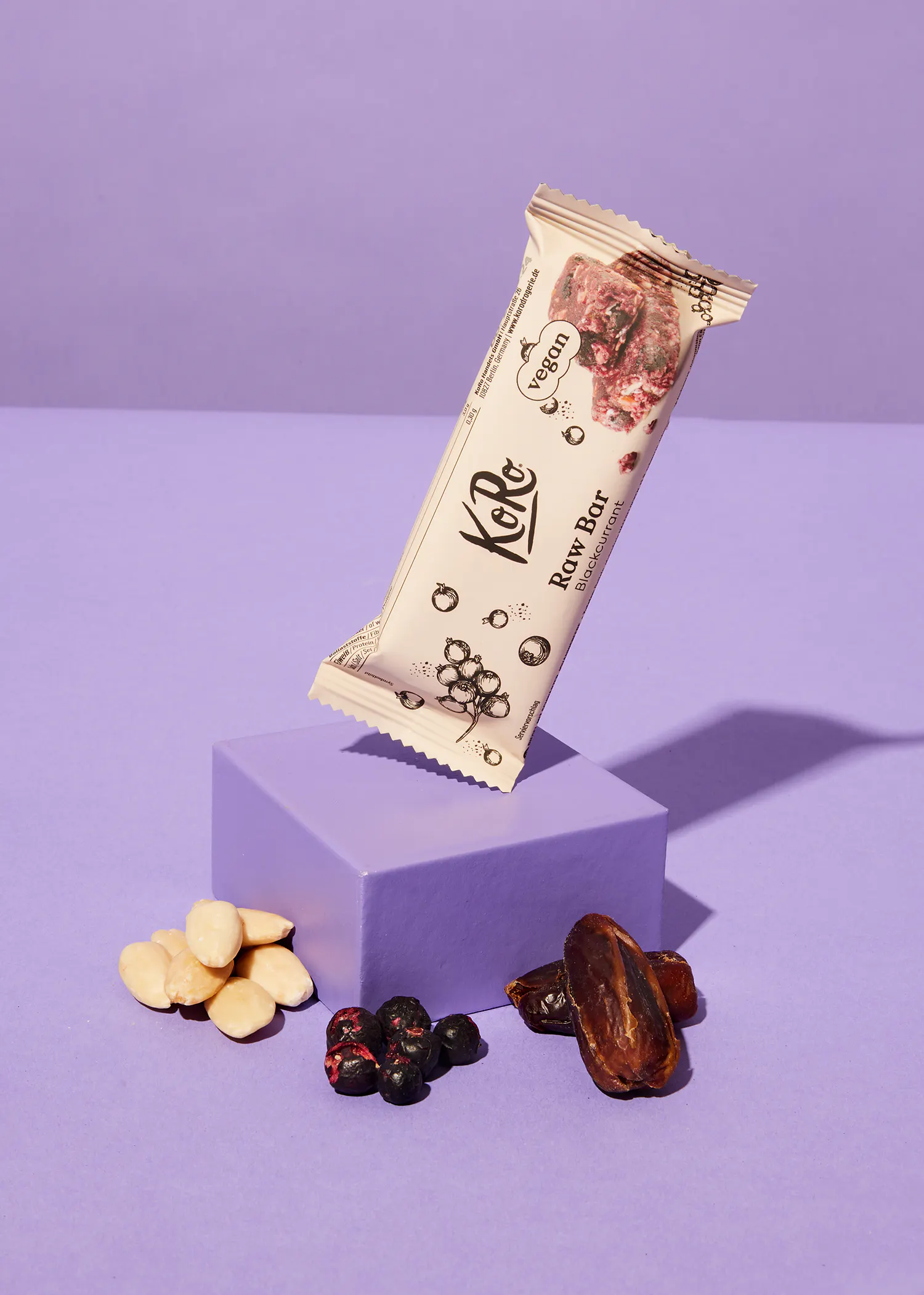 une barre végétalienne posée sur un bloc violet entourée de fruits et de noix