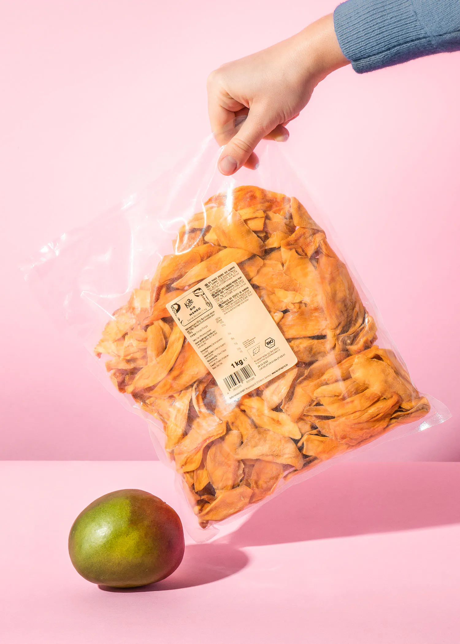 une personne tient un sac de fruits séchés à côté d' une mangue