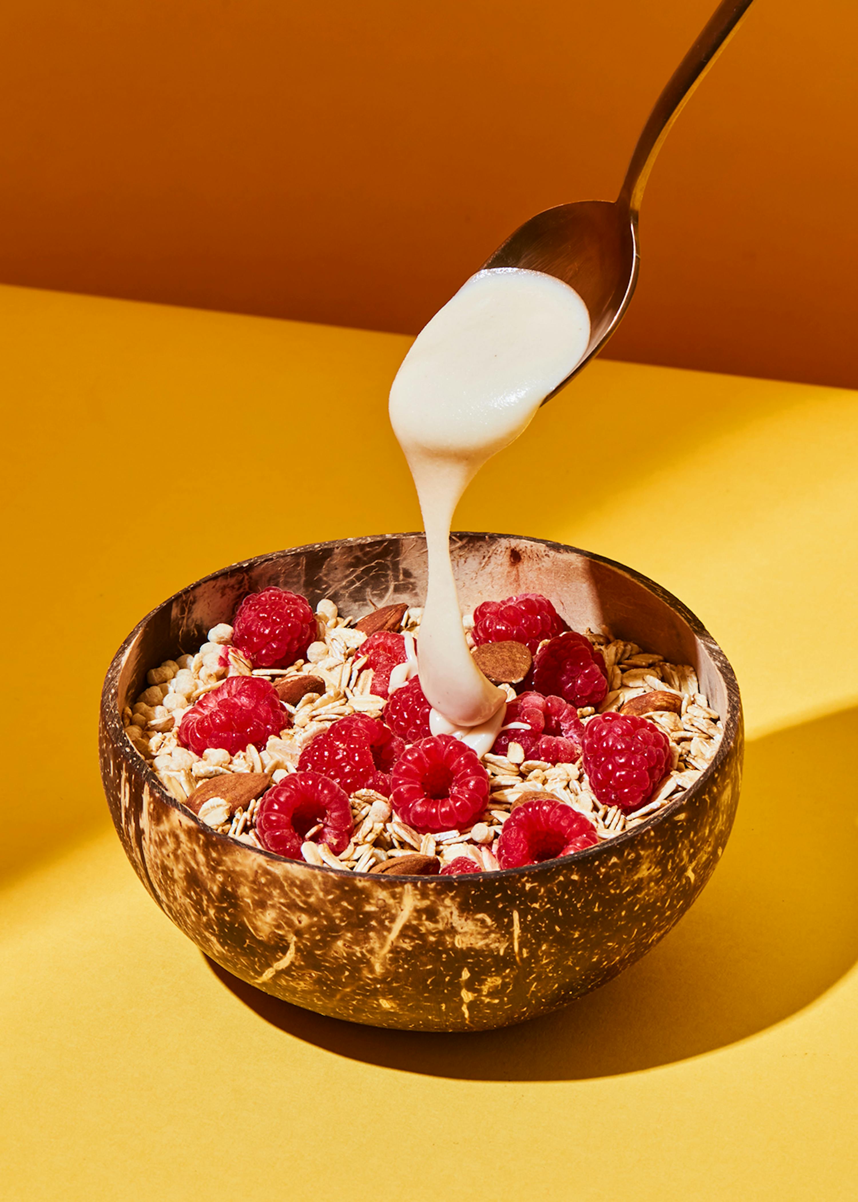 a bowl of cereal with raspberries and almonds is being poured with a spoon