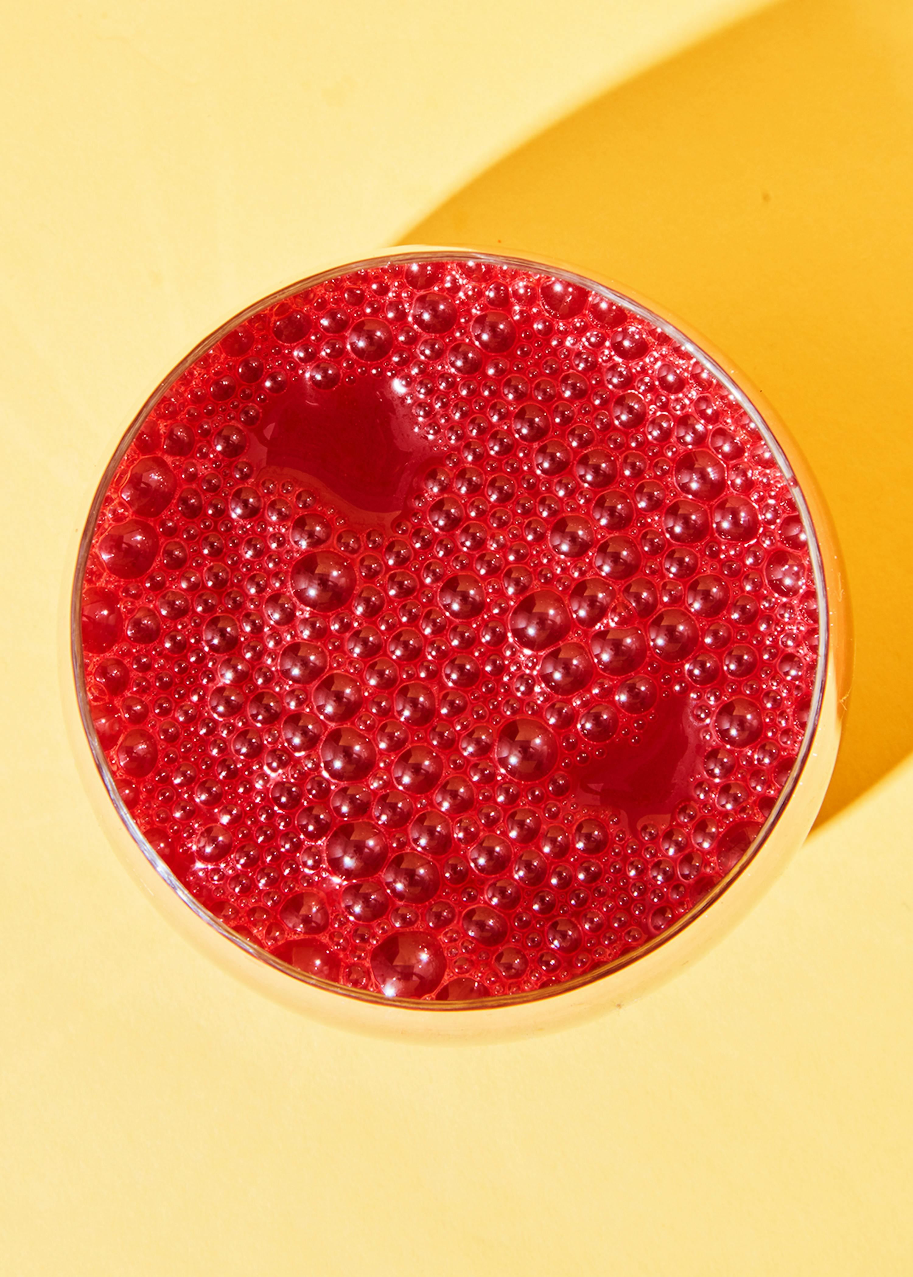 un primo piano di un bicchiere di bevanda rossa su sfondo giallo