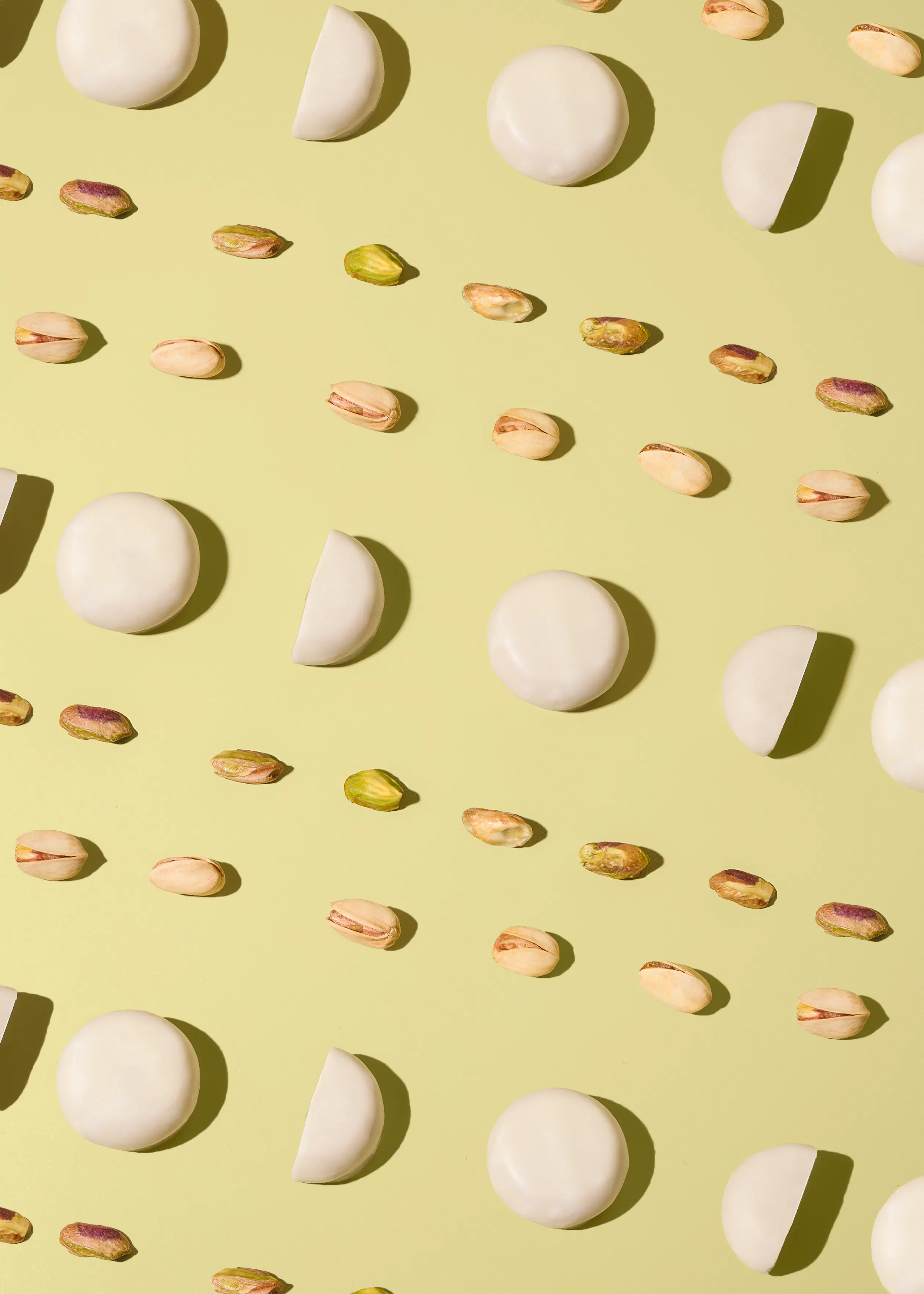 un motif de bonbons ronds et demi-ronds blancs et de pistaches entières et décortiquées sur un fond vert clair.