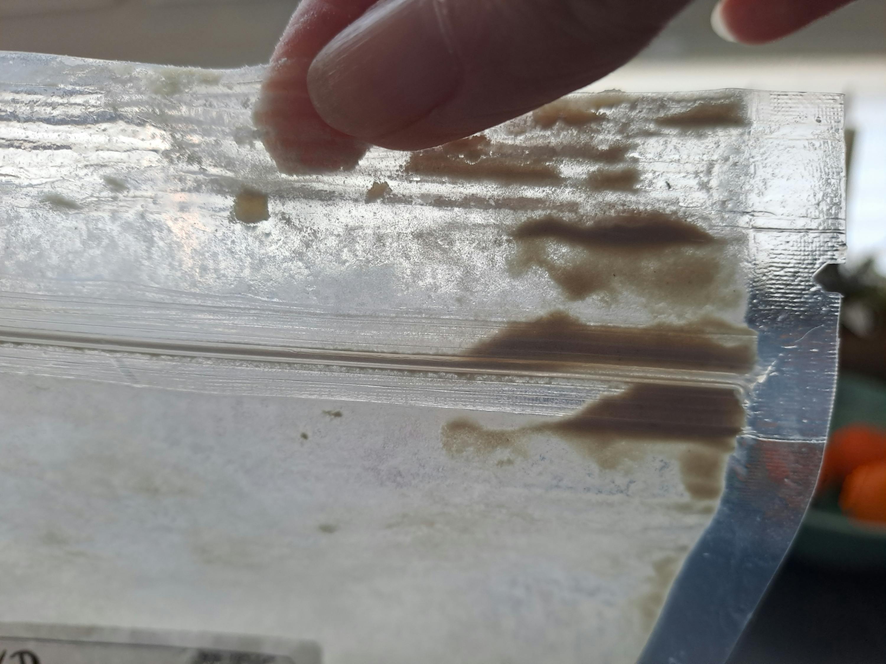 a clear plastic bag containing a light powdery substance with darker, clumpy areas, held by a finger.