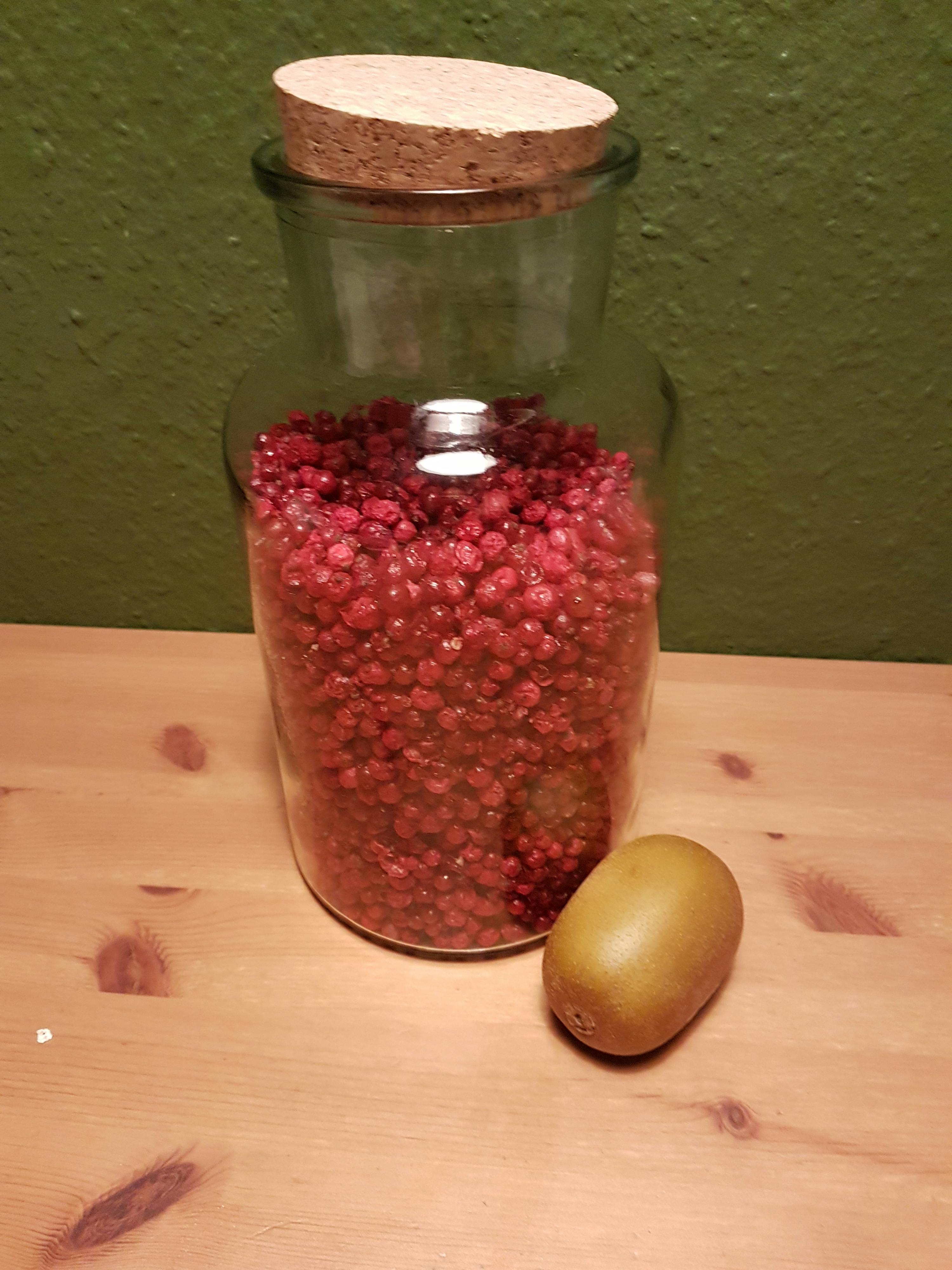 a jar filled with pink peppercorns next to a kiwi