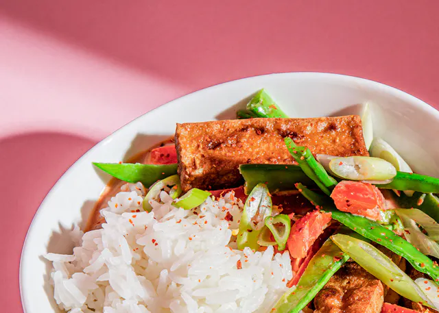 a bowl of rice and vegetables on a pink background