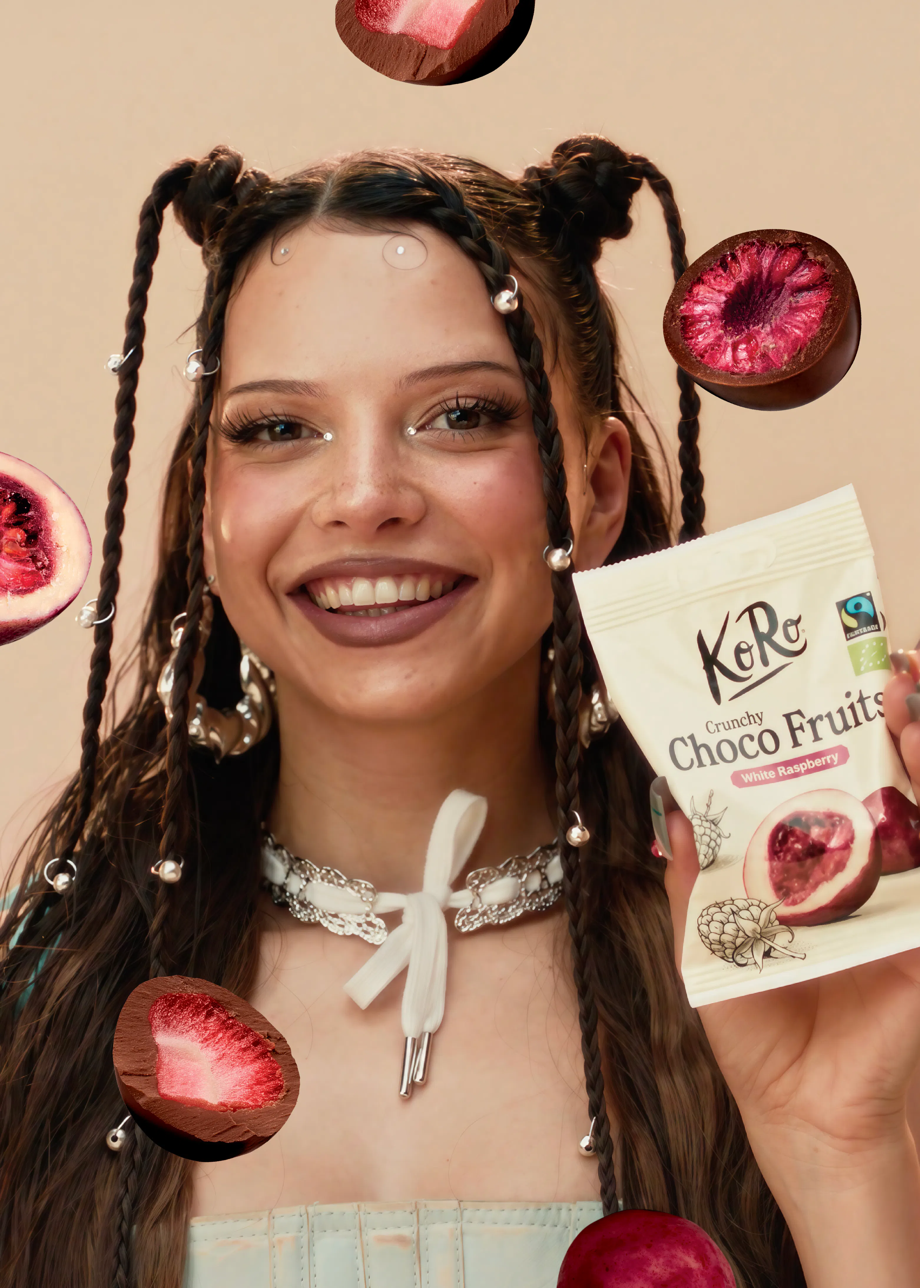 une jeune femme souriante tient un sachet de fruits enrobés de chocolat koro entourée de framboises et de fraises enrobées de chocolat flottant dans les airs.