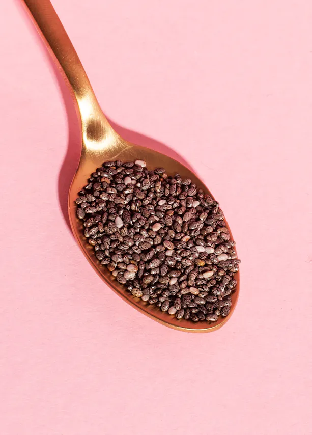 une cuillère remplie de graines de chia sur un fond rose