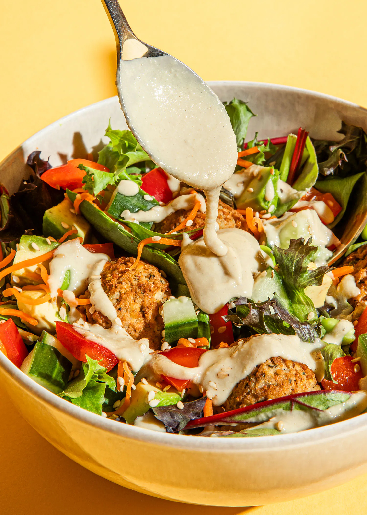 une cuillère verse une sauce sur une salade de légumes