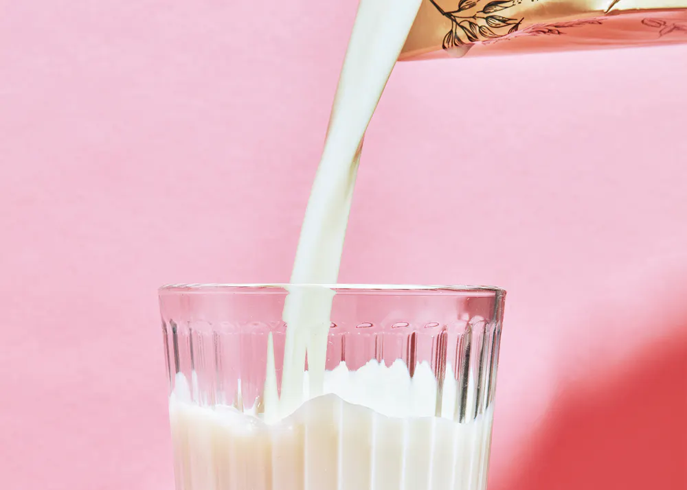 du lait est versé dans un verre sur fond rose