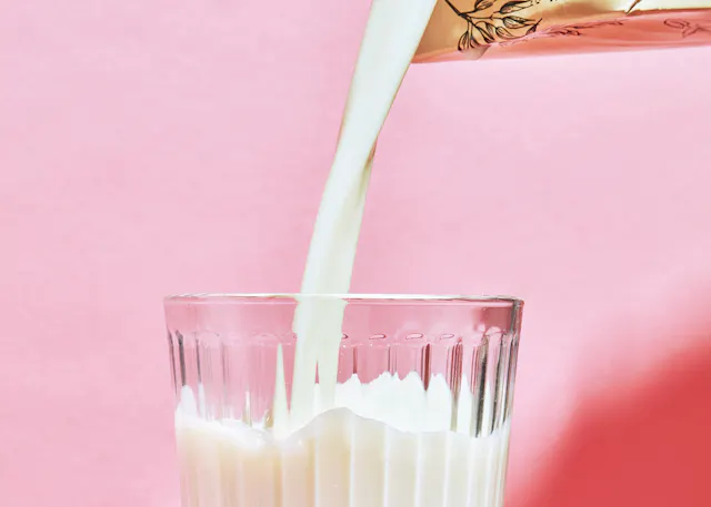 Milch wird in ein Glas gegossen und auf einem rosa Hintergrund