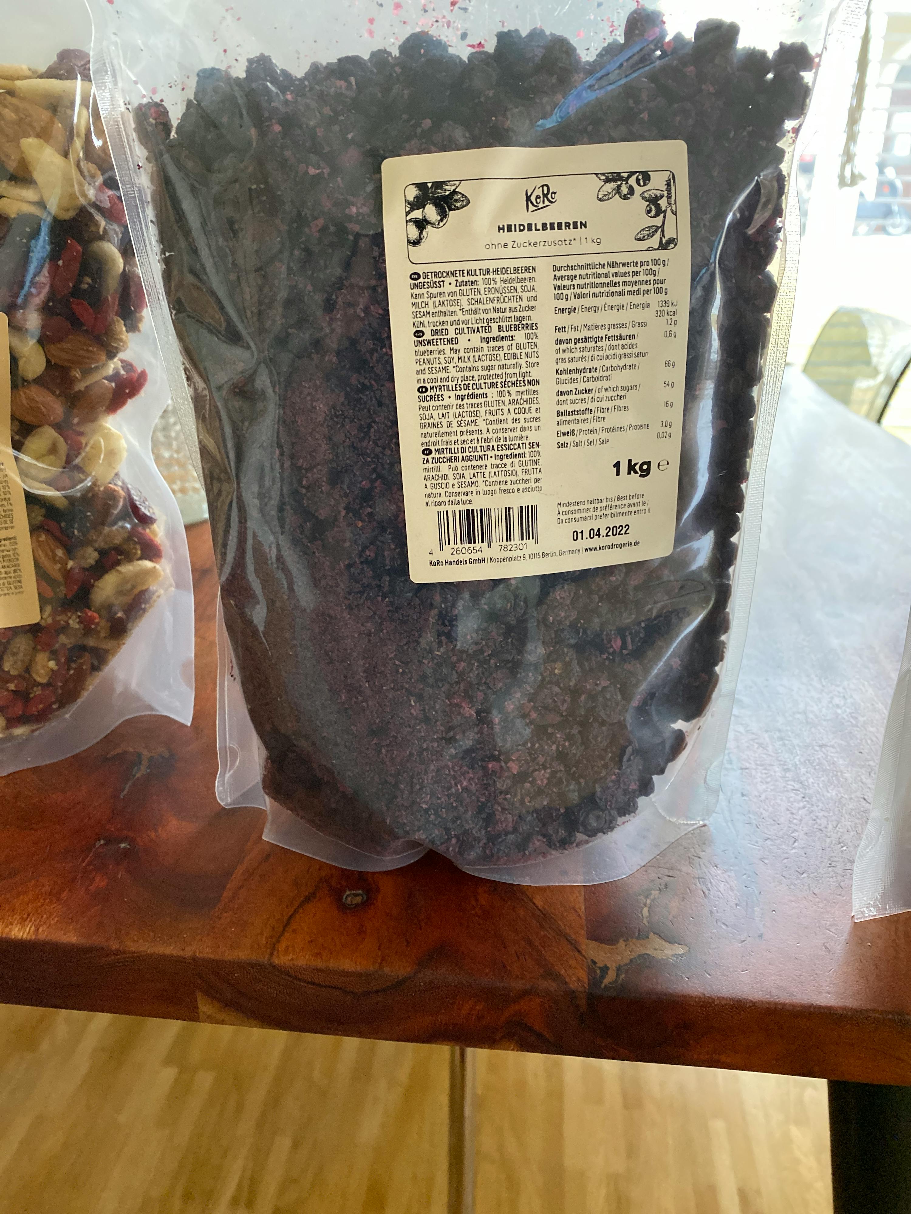 a bag of dried cranberries sits on a wooden table next to a bag of nuts