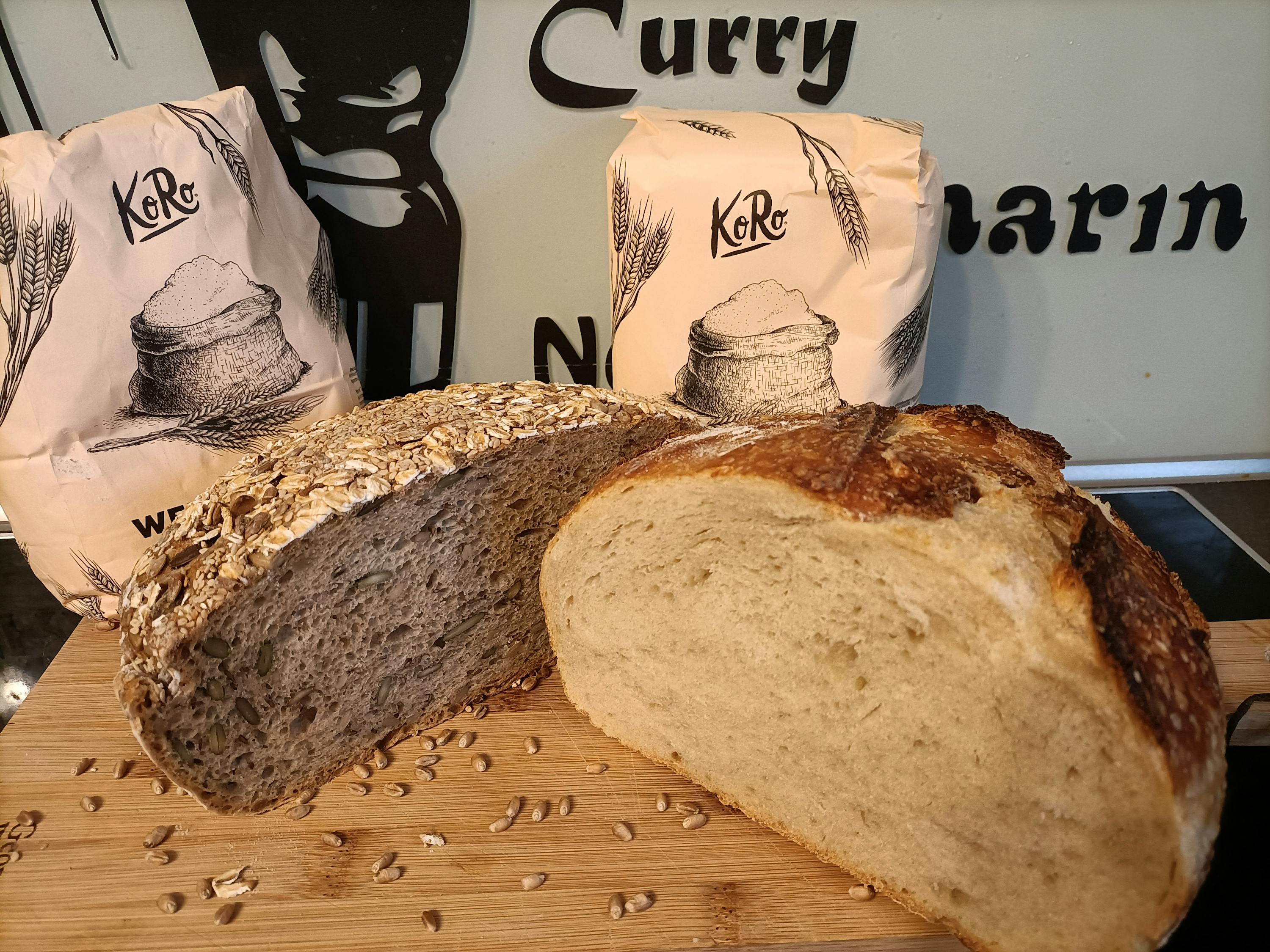 a loaf of bread sits on a wooden cutting board next to two bags of kore wheat flour