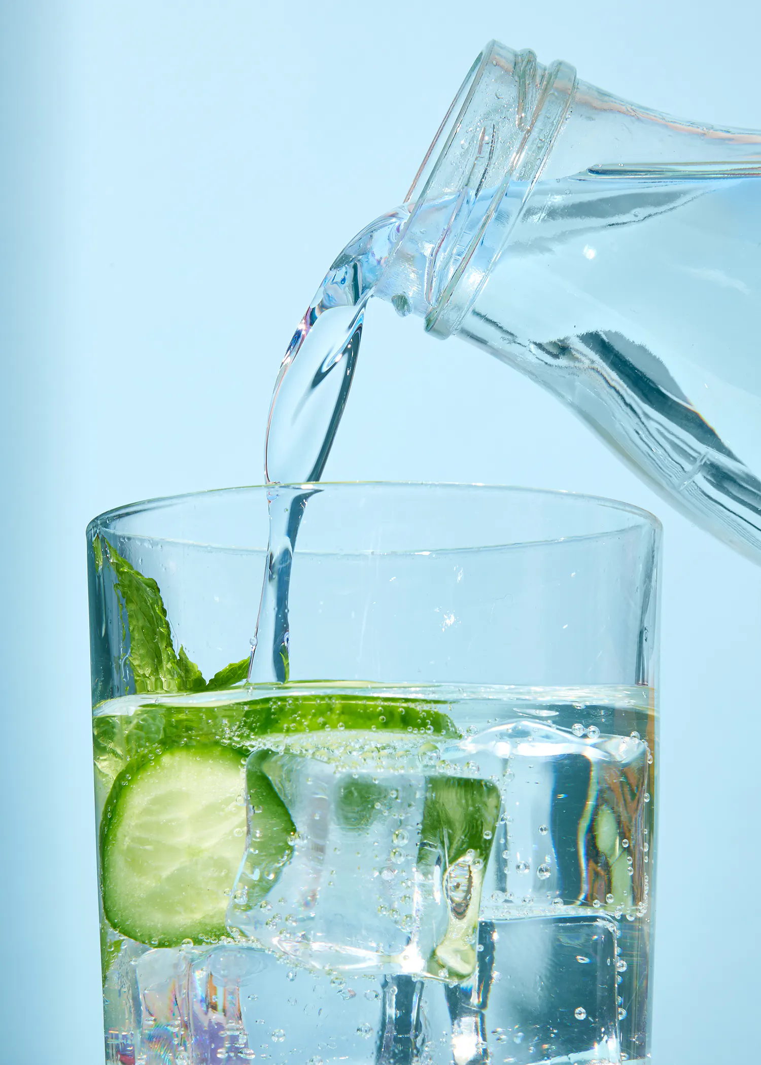 Wasser wird in ein Glas mit Eiswürfeln und einer Gurke gegossen