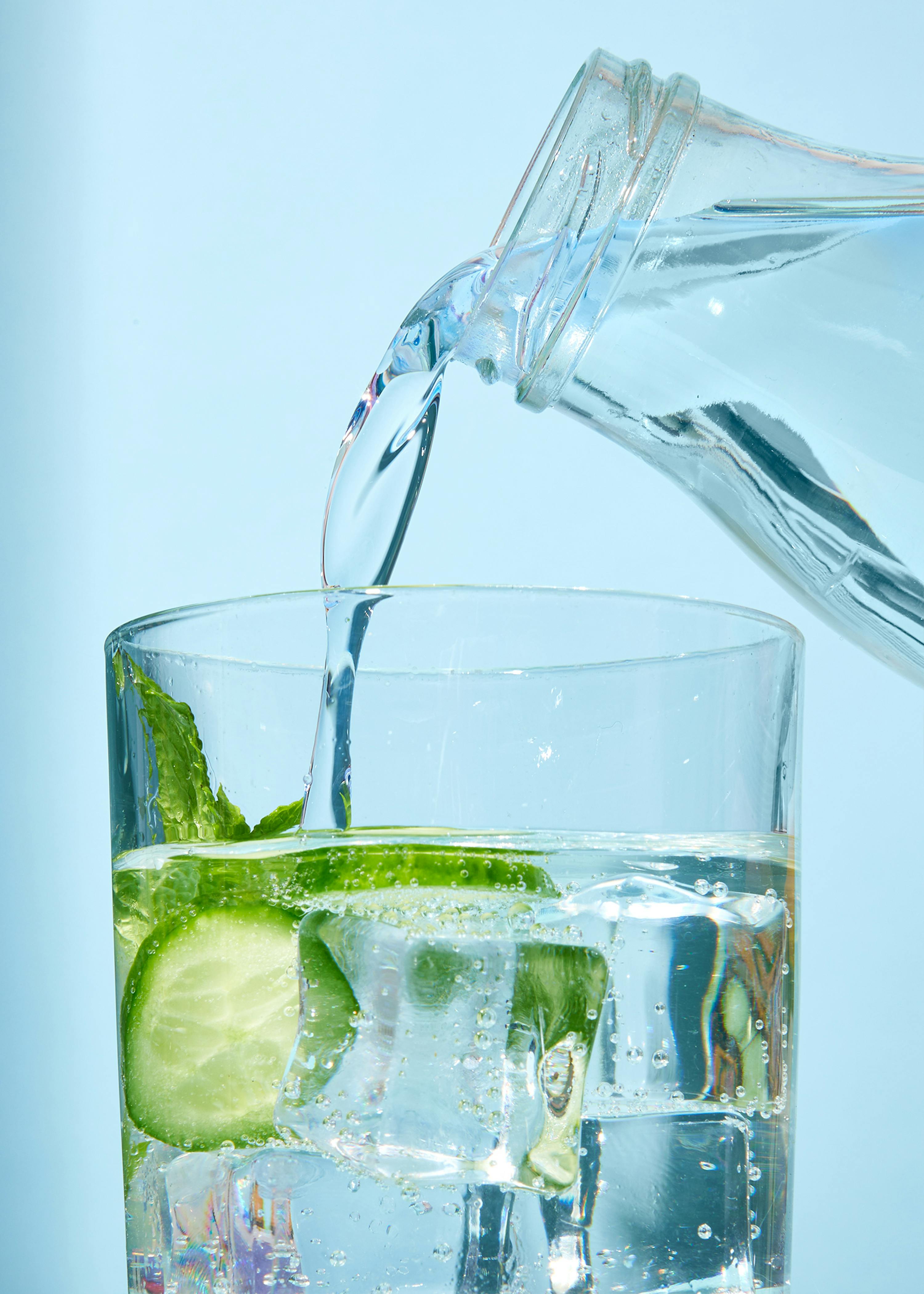 water is being poured into a glass with ice cubes and cucumber slices