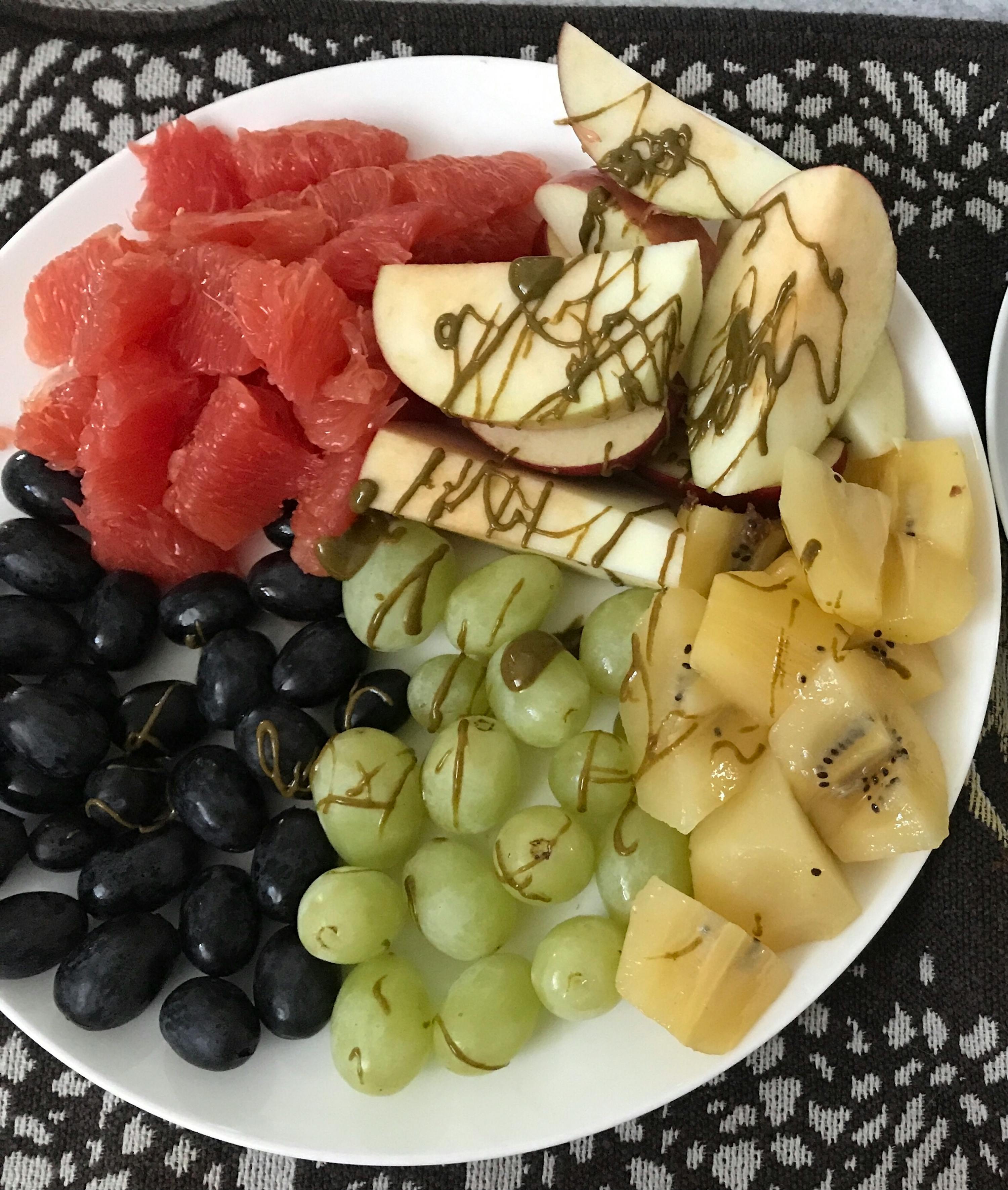 une assiette blanche remplie de raisins , pomelos , pommes et kiwis