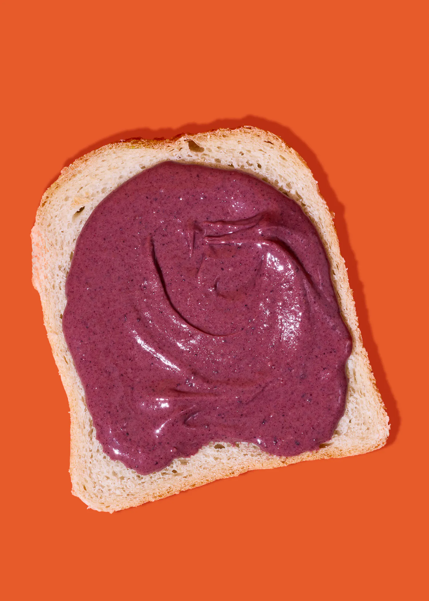 ein stück weißbrot mit einer dicken schicht lila fruchtmus auf einem leuchtend orangefarbenen hintergrund.
