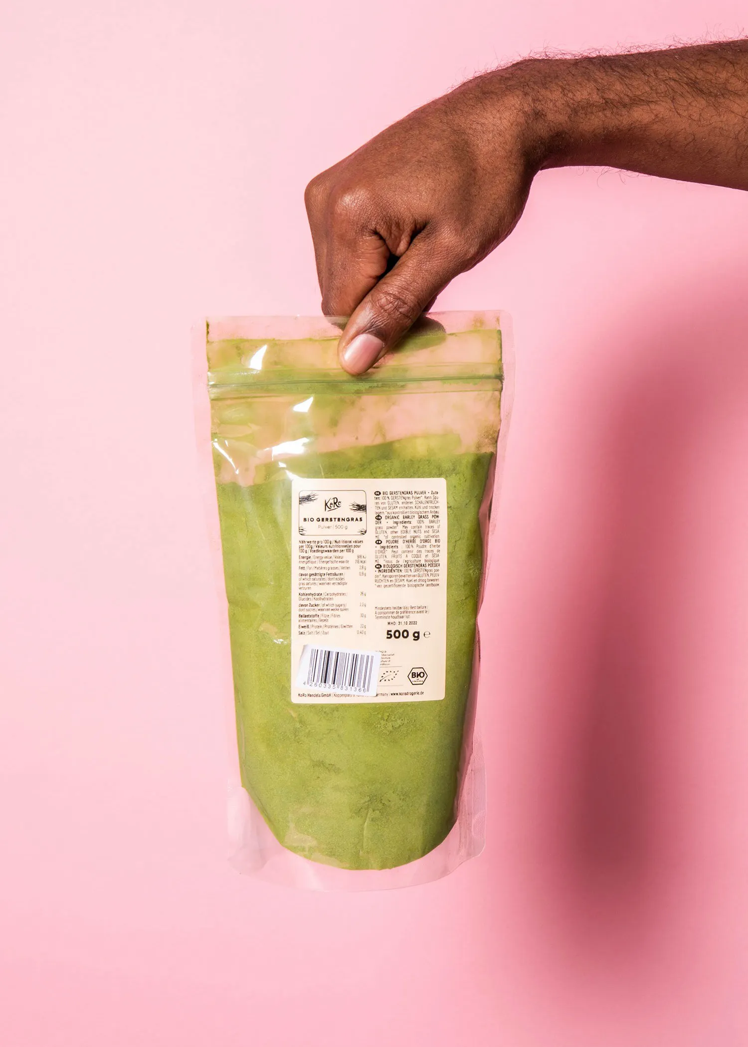 une personne tient un sac de poudre de matcha sur un fond rose