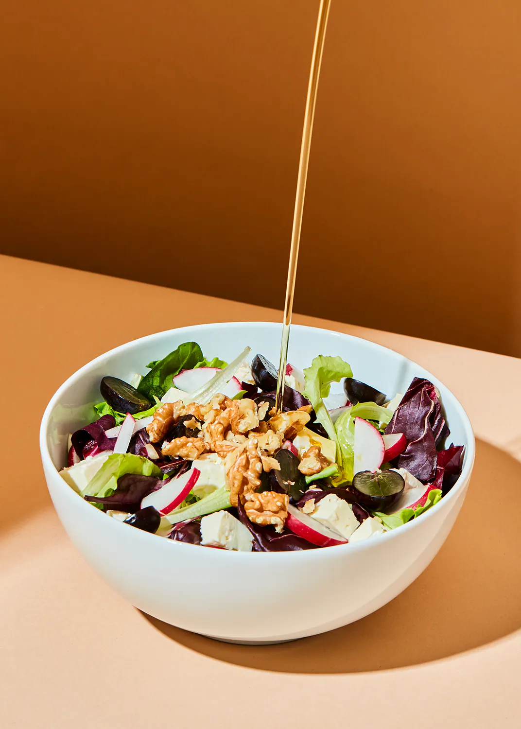 a salad with nuts and grapes is being poured with olive oil
