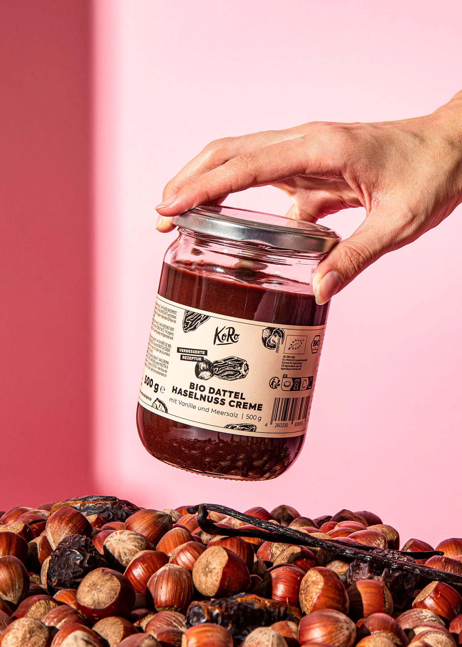 une personne tient un bocal de pâte à tartiner sur une pile de noisettes