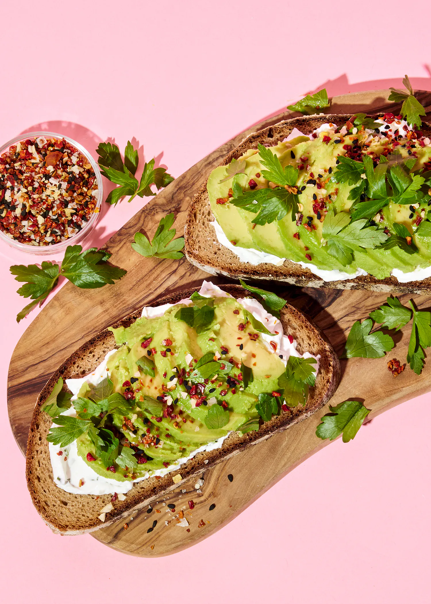 two slices of toast with avocado and sour cream on a wooden cutting board