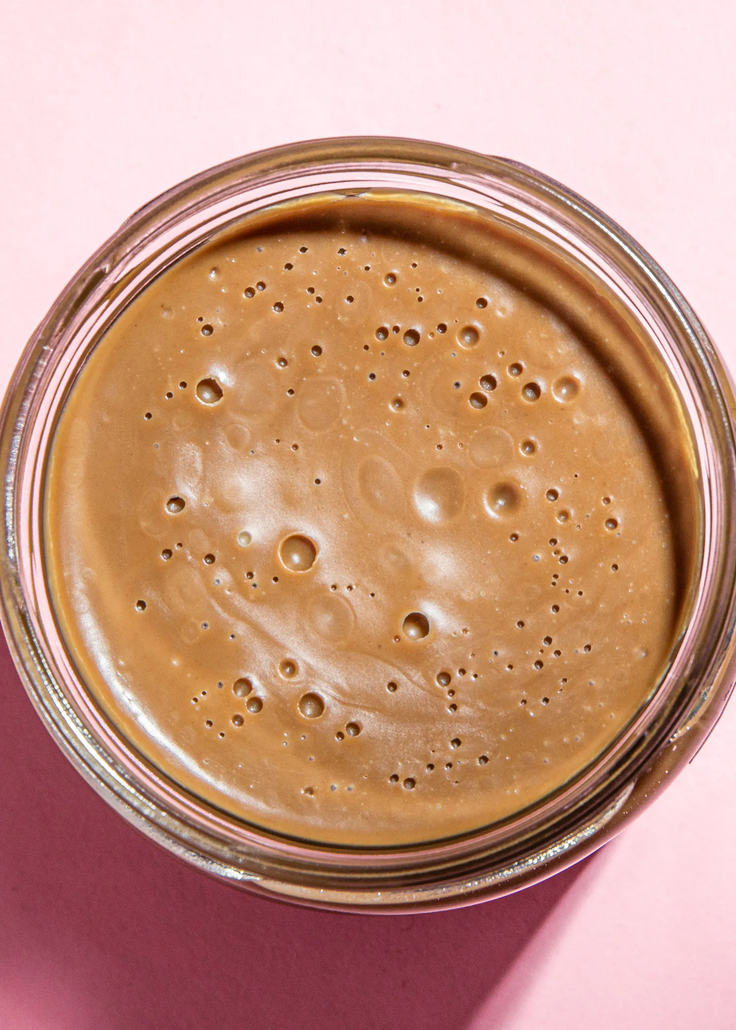 un bocal en verre rempli d' un liquide brun sur fond rose