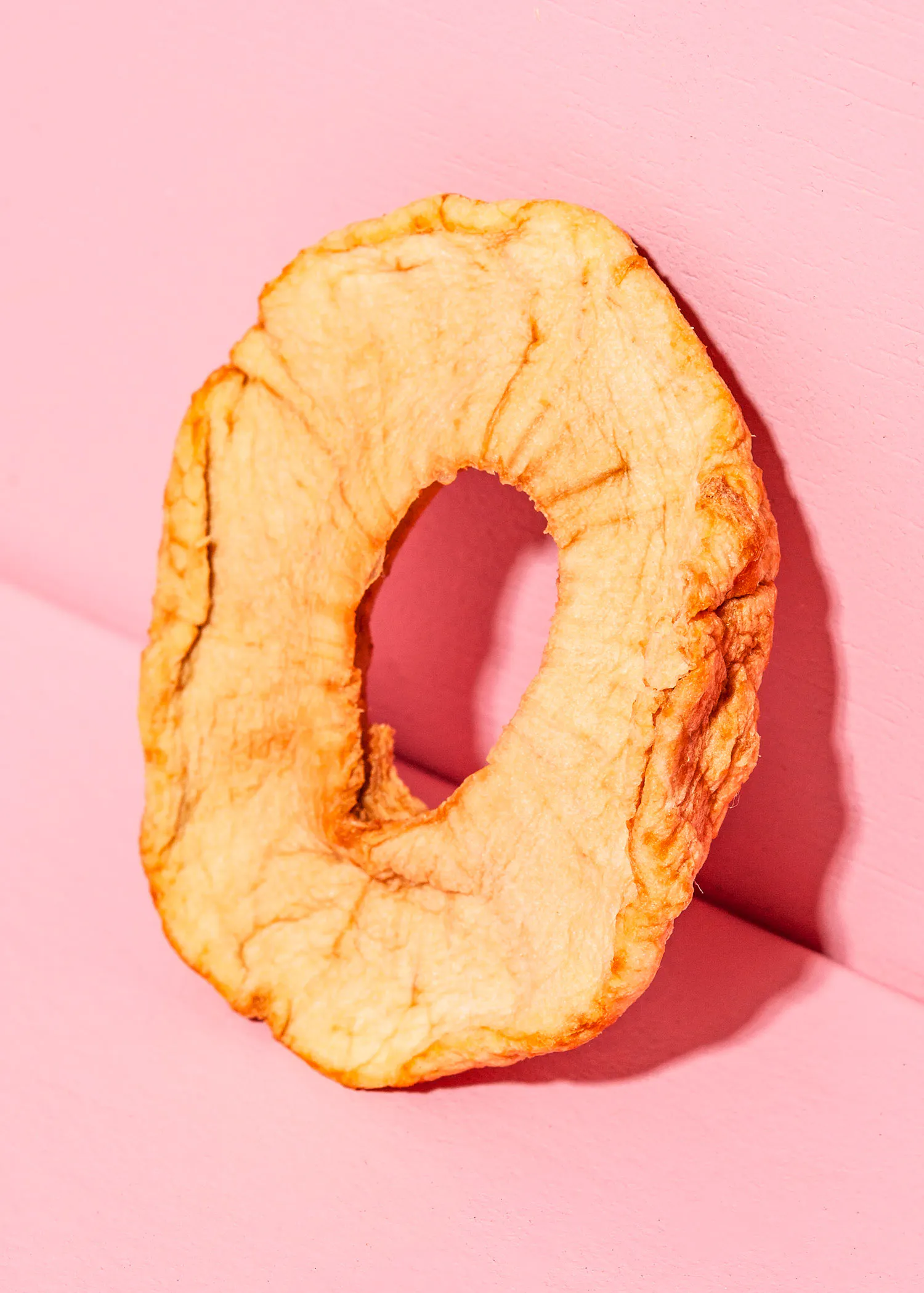 an apple slice with a hole in the middle on a pink background