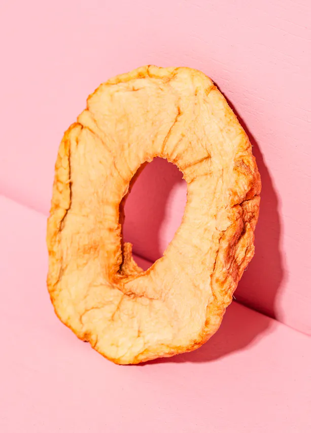 an apple slice with a hole in the middle on a pink background