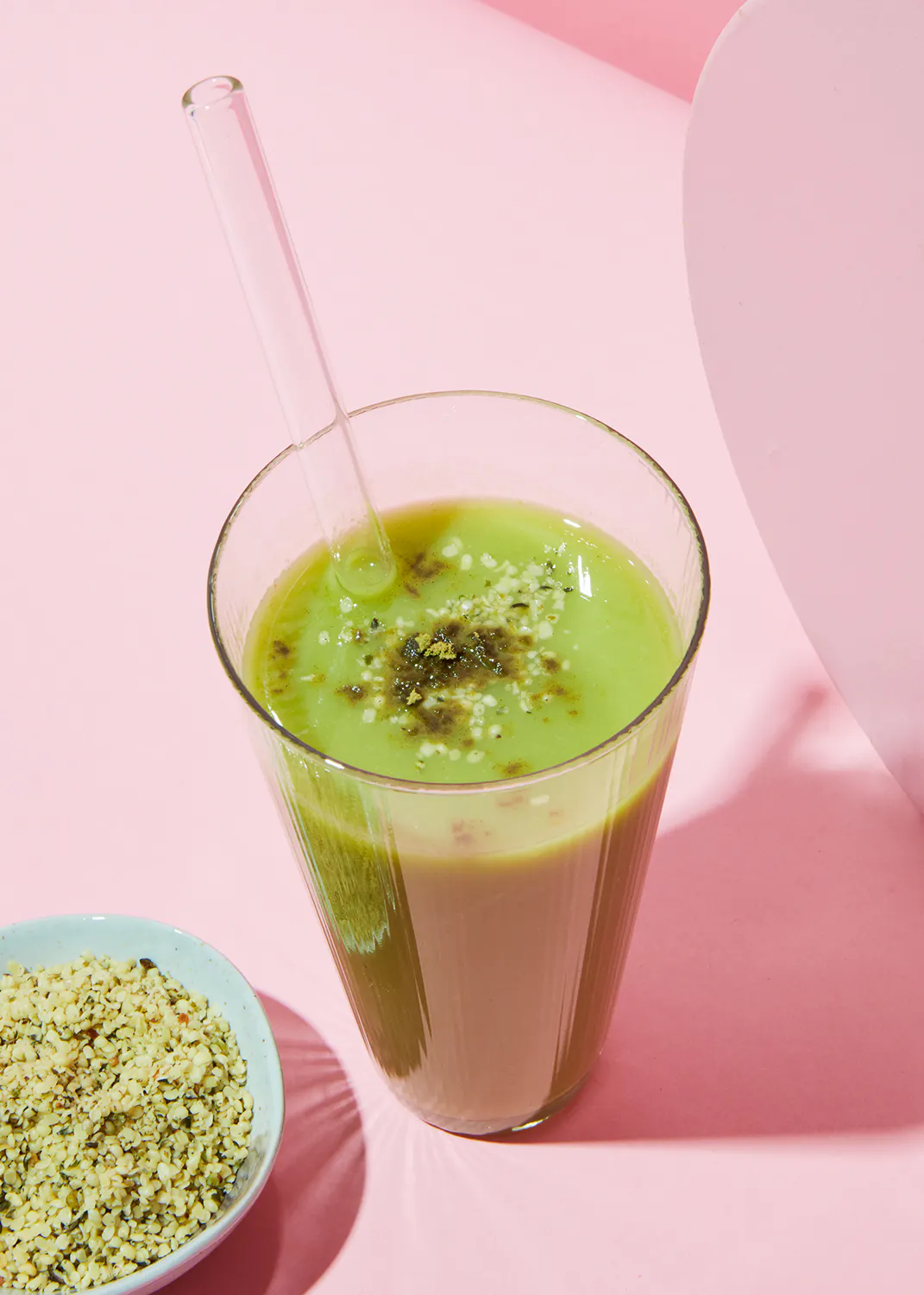 a green smoothie in a glass with a straw next to a bowl of hemp seeds