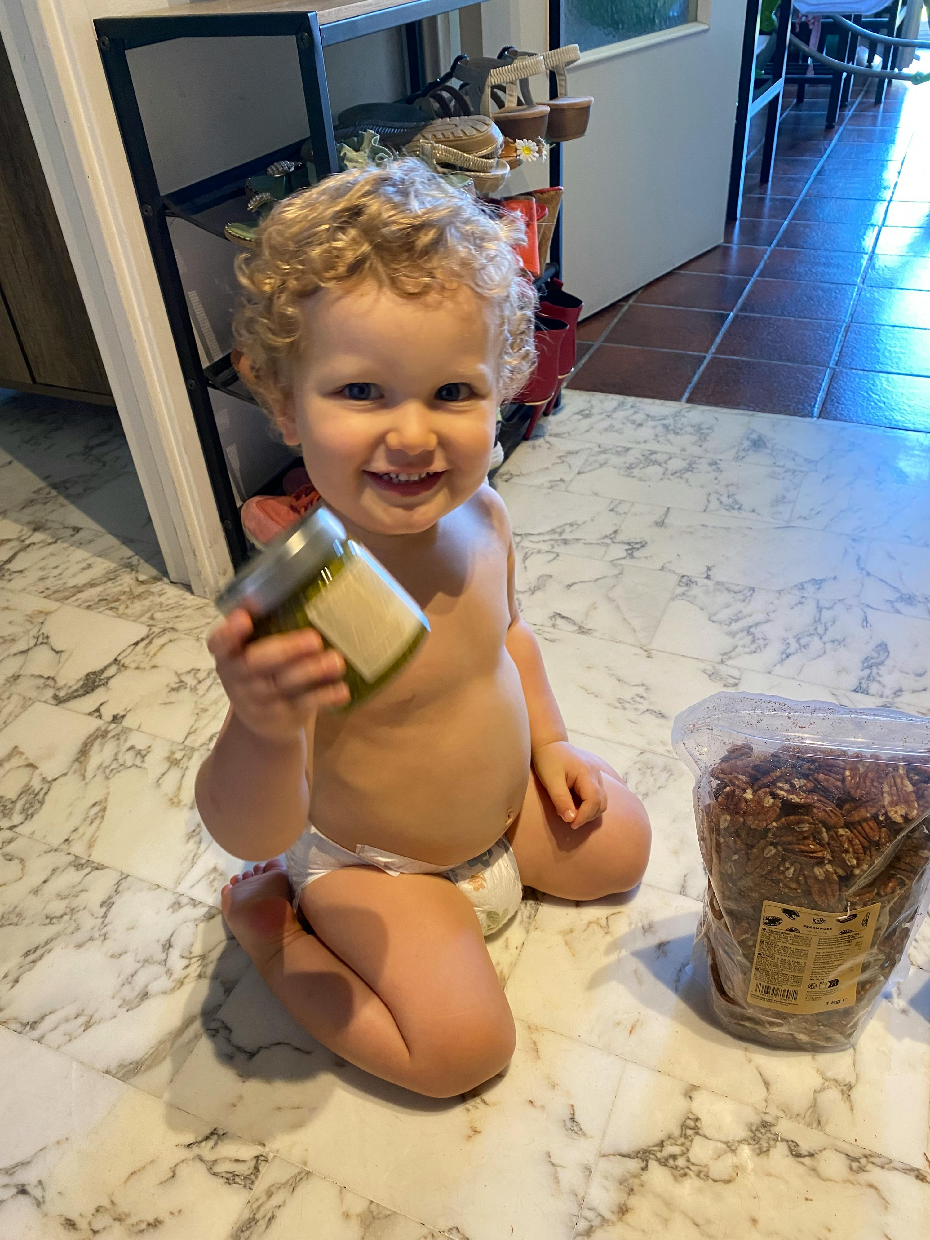 ein Baby in einer Windel sitzt auf einem Marmortisch und hält eine Dose Olivenöl