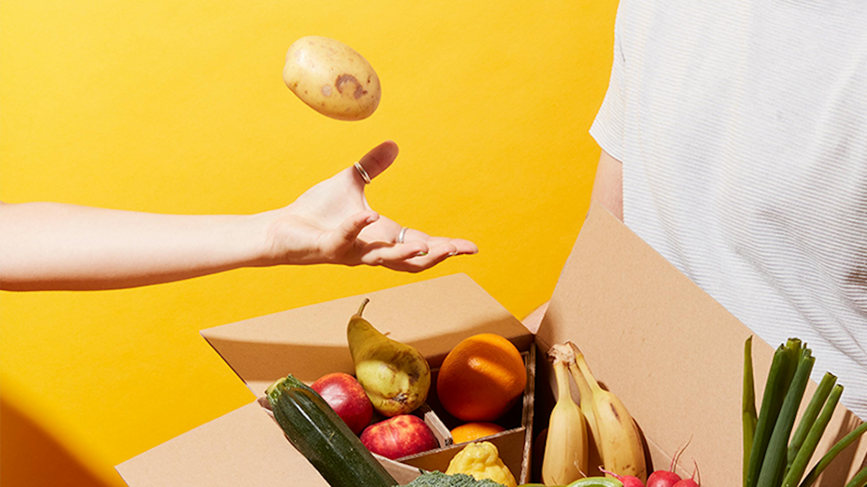 a person throwing a potato into a box full of fruits and vegetables
