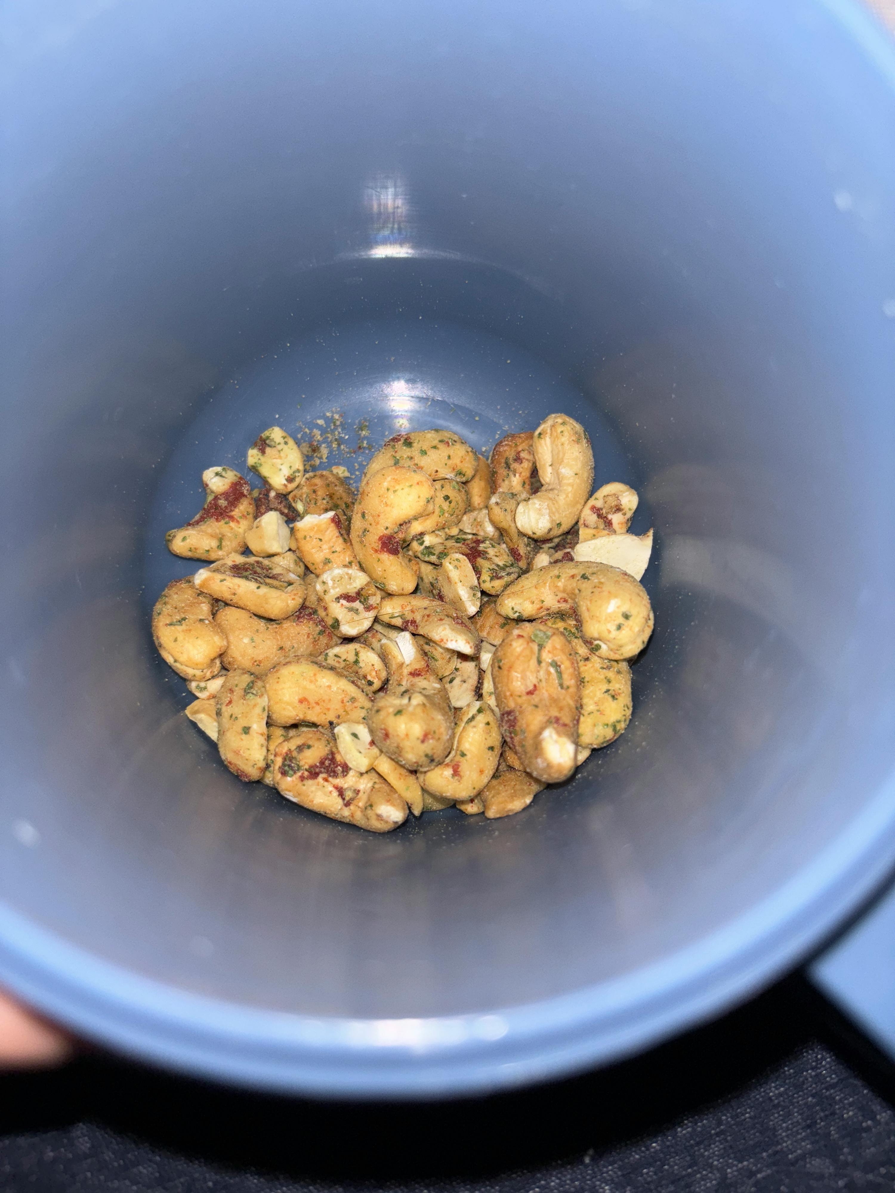 seasoned cashews with red and green spices are at the bottom of a blue cup.