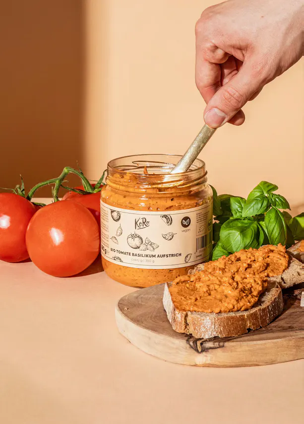 eine Person hält einen Löffel in einem Glas mit Tomatenpesto darauf