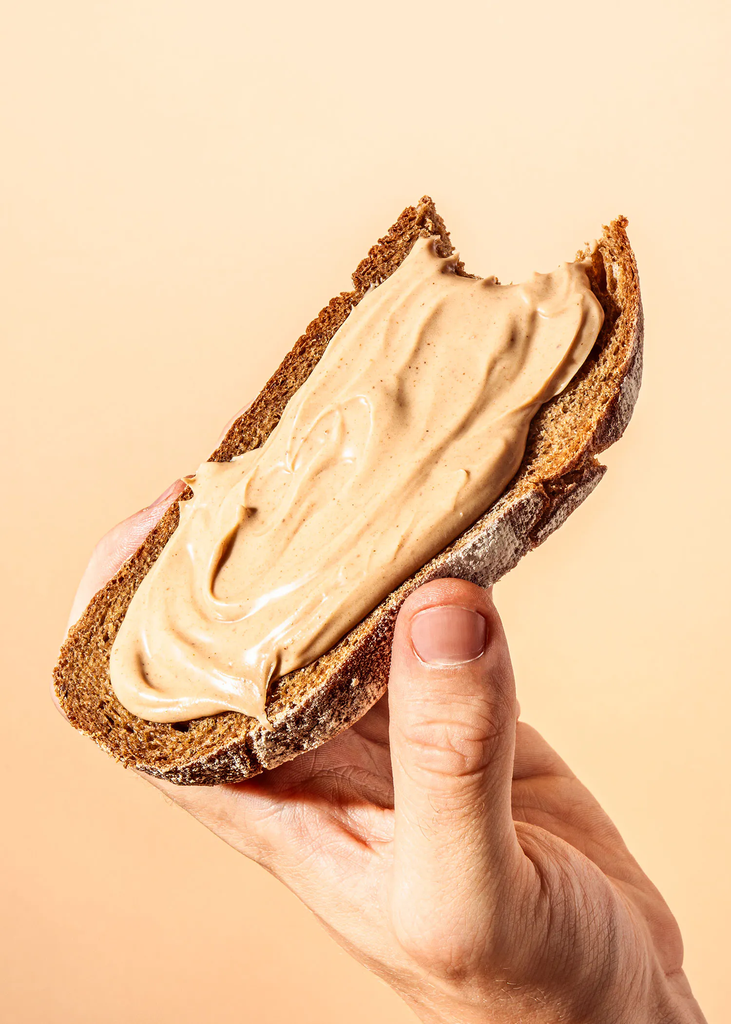 eine Hand hält ein Stück Brot mit Erdnussbutter darauf