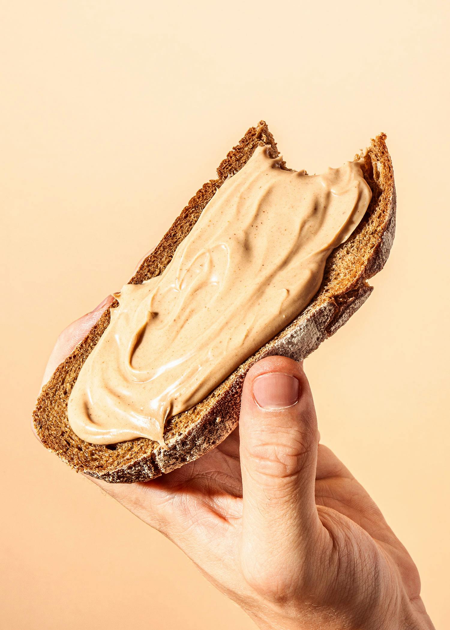 eine Hand hält ein Stück Brot mit Erdnussbutter darauf