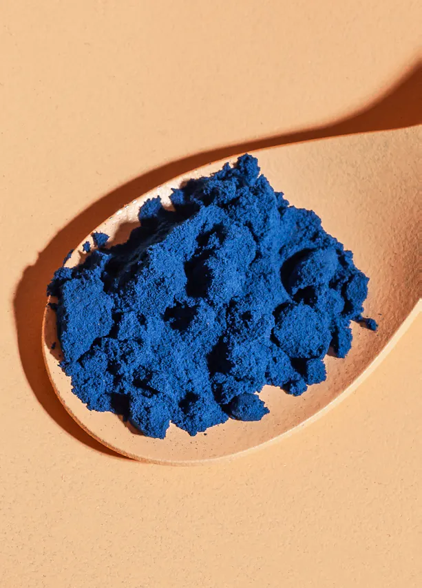 une cuillère en bois remplie de poudre bleue sur une surface orange