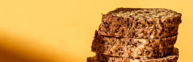 ein stapel scheiben aus dunklem körnerbrot vor einem gelben hintergrund.