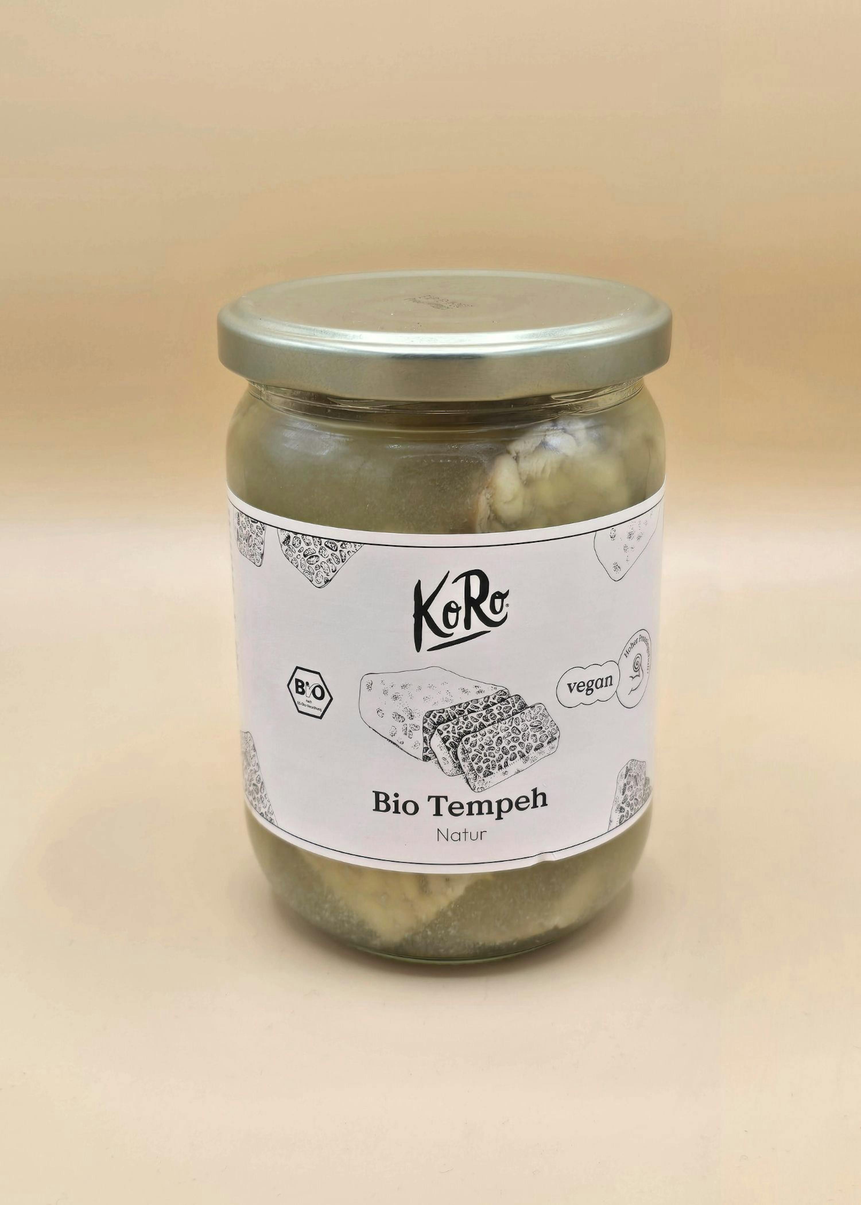 un barattolo di vetro con coperchio argentato contenente tempeh biologico naturale del marchio koro, con etichette bio e vegan.