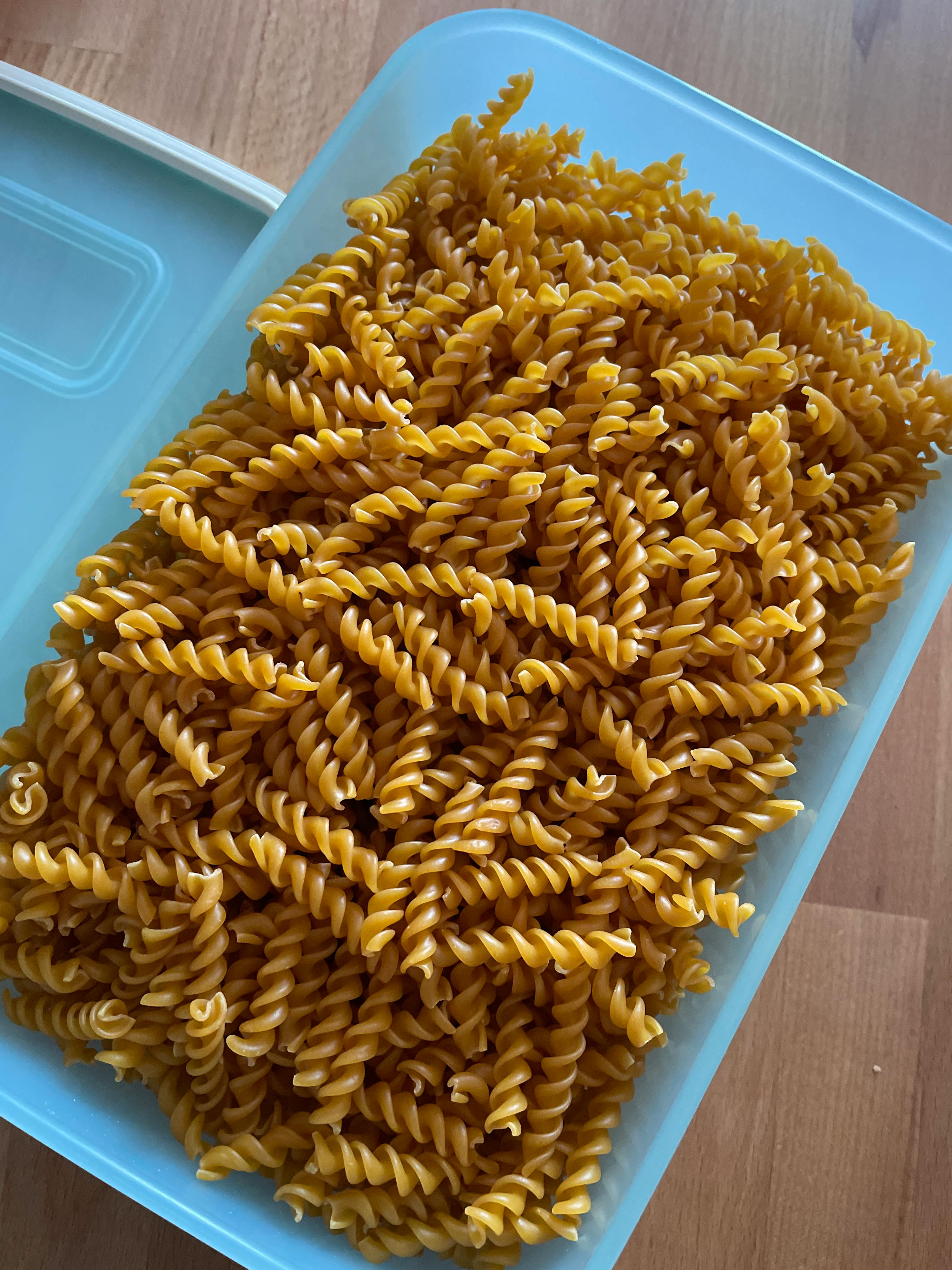 a plastic container filled with spiral pasta on a wooden table