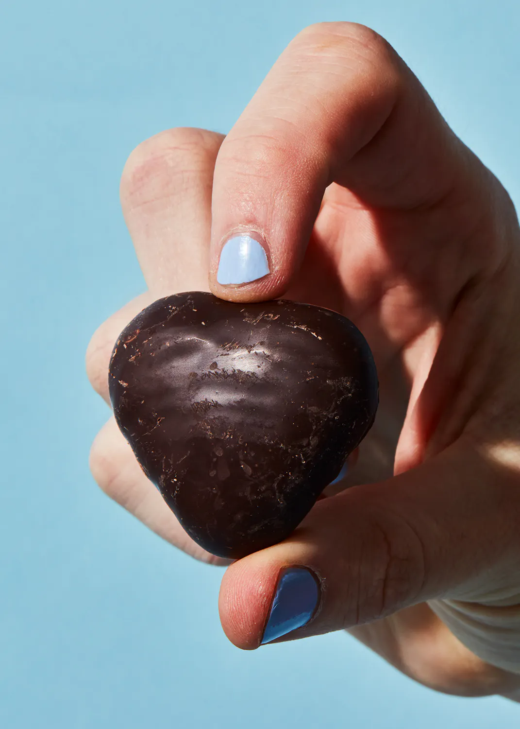 a hand with blue nail polish is holding a heart shaped chocolate